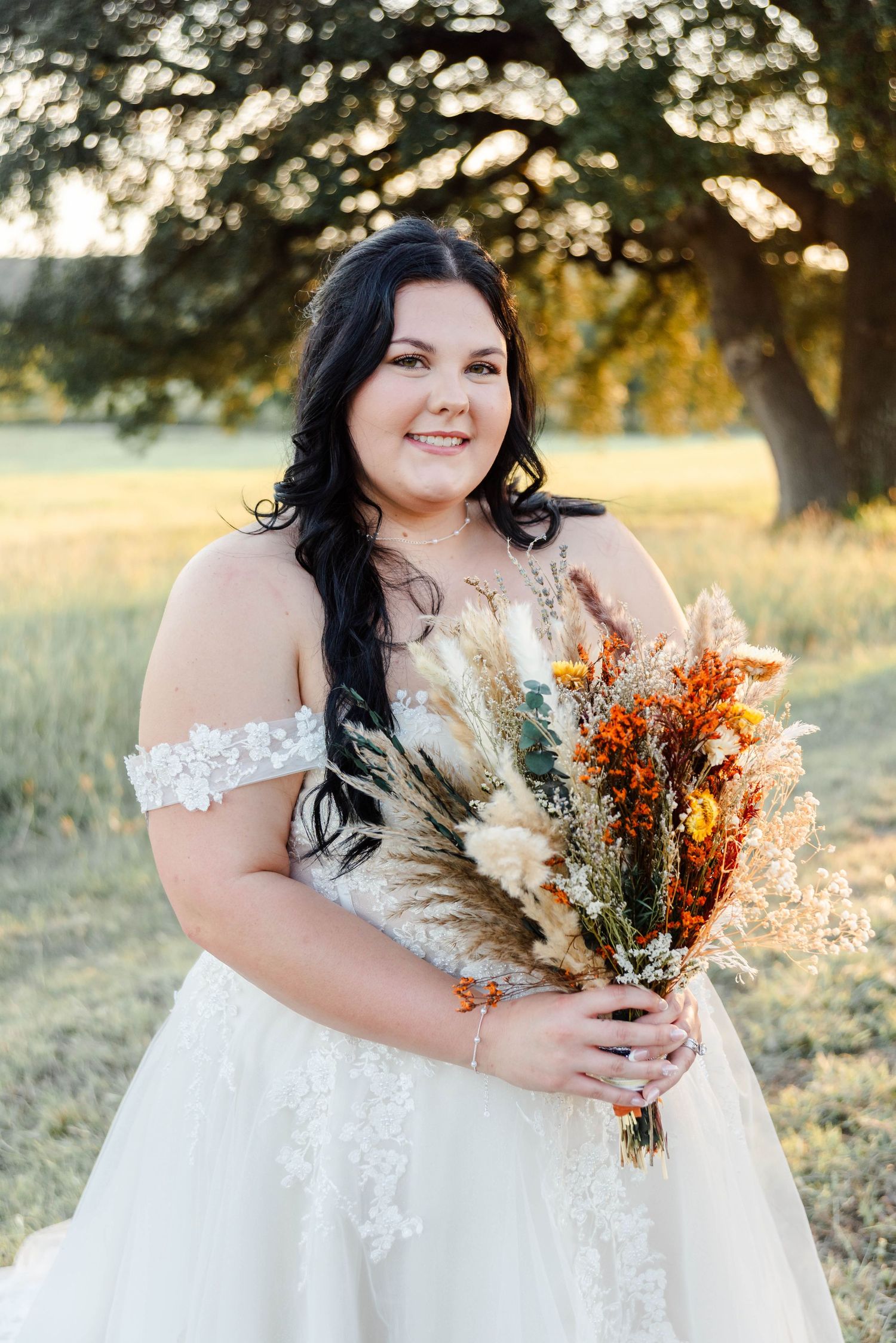 bride holding a floral bouquet in a field smiling