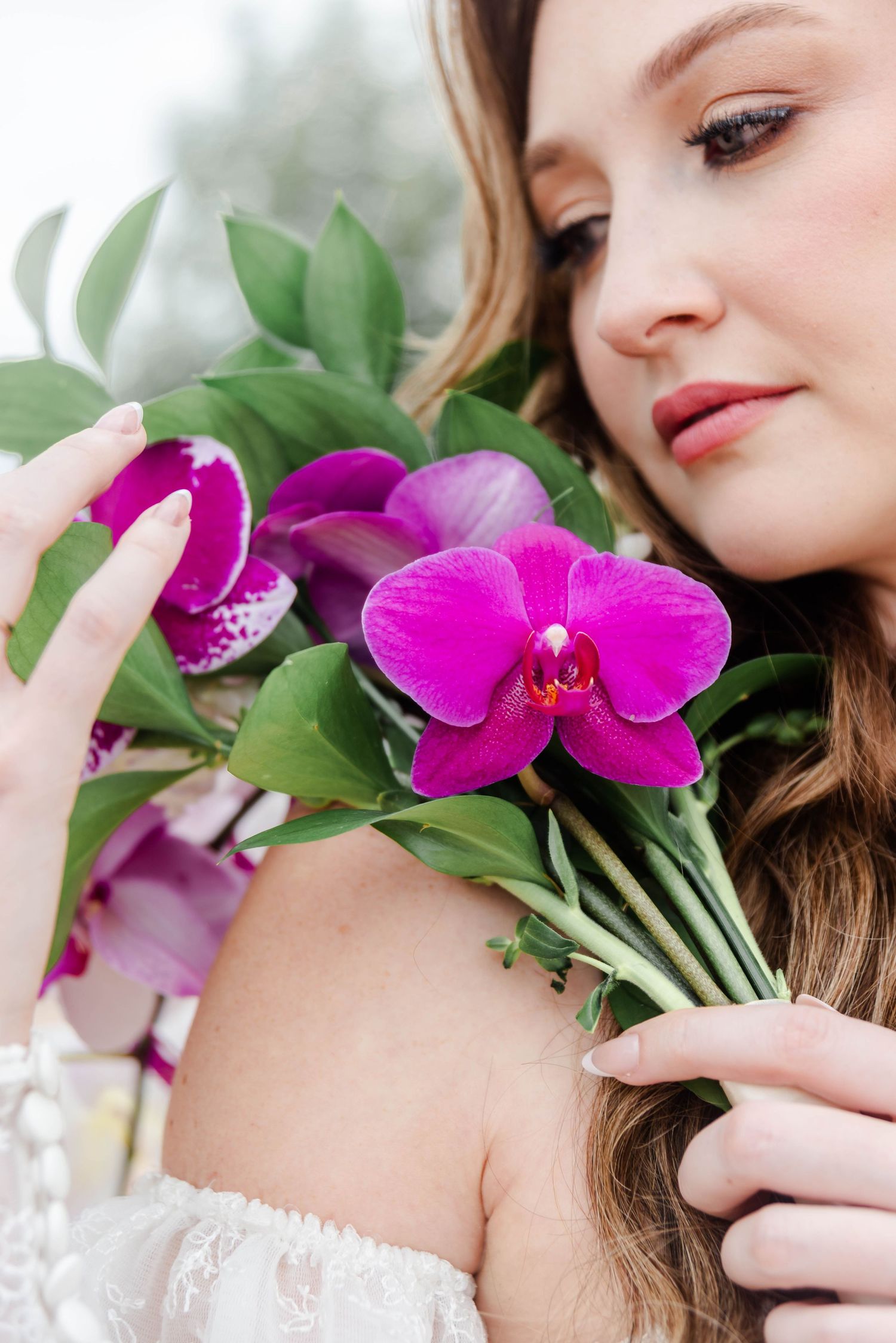 A bride holds her flowers over her shoulder gazing at them