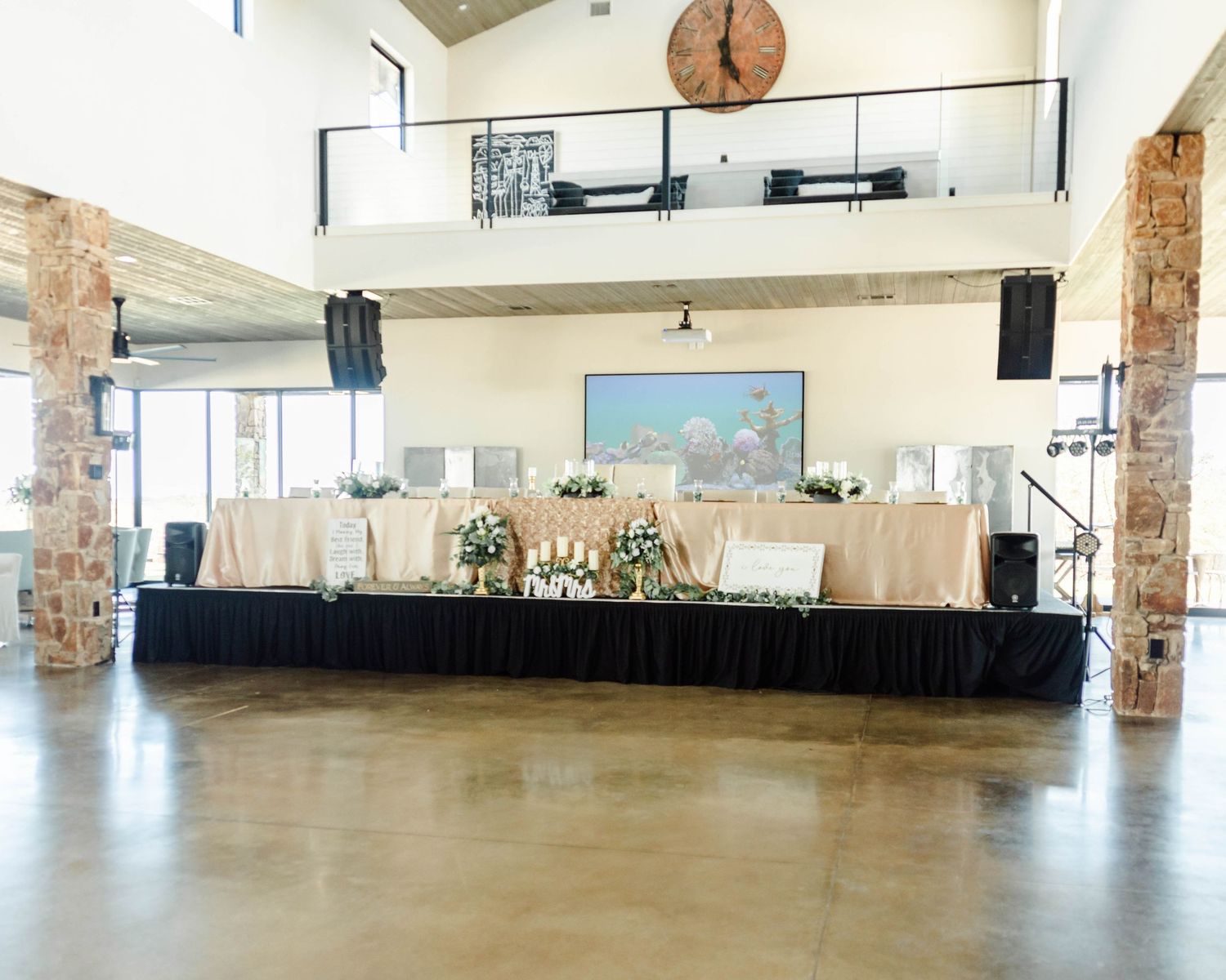 A modern event space with stone pillars, a raised black stage platform, and coastal artwork on the wall.