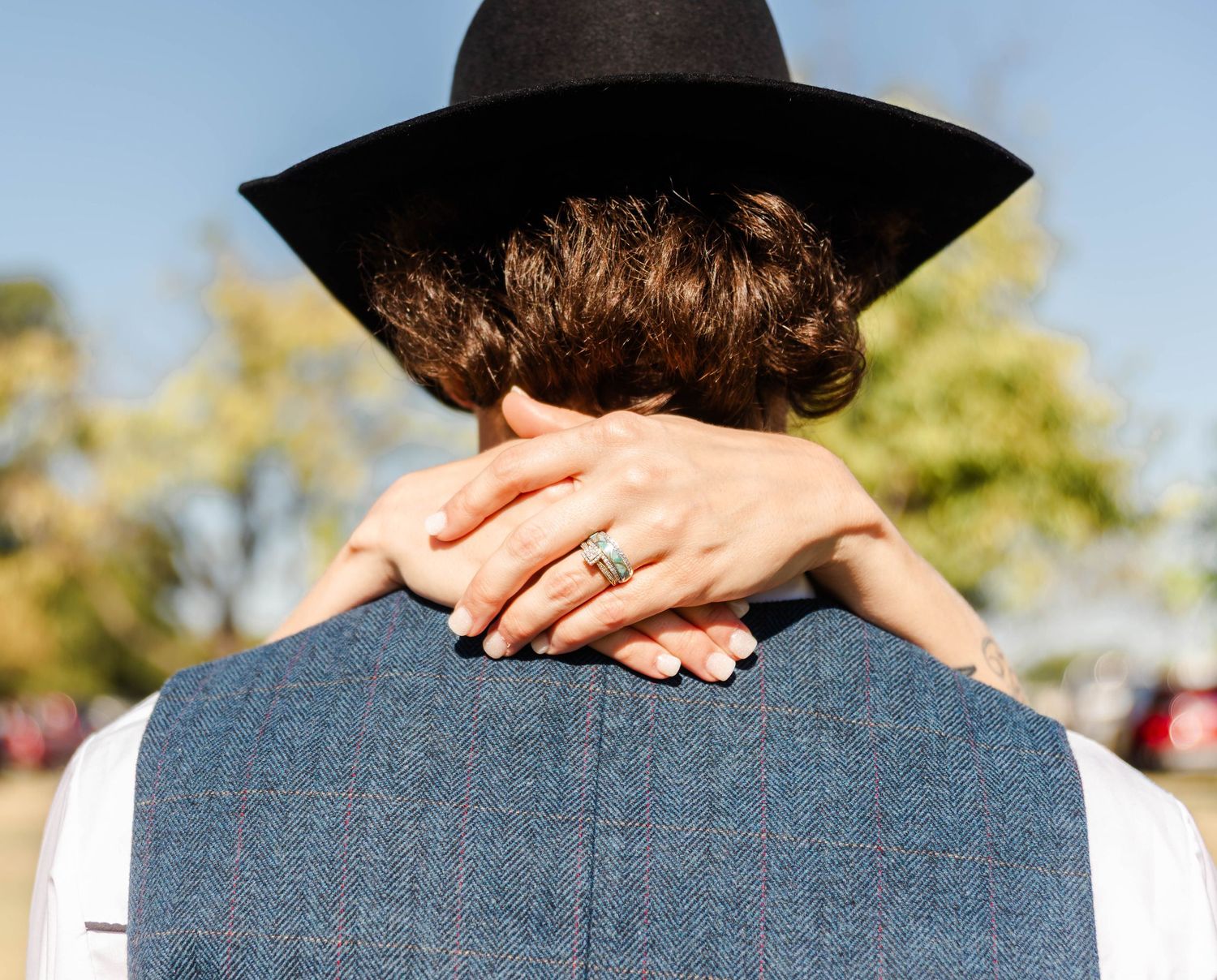 A bride has her hands gently set behind the grooms neck. The groom is wearing a cowboy hat with the focus on the bride's hand and rings.