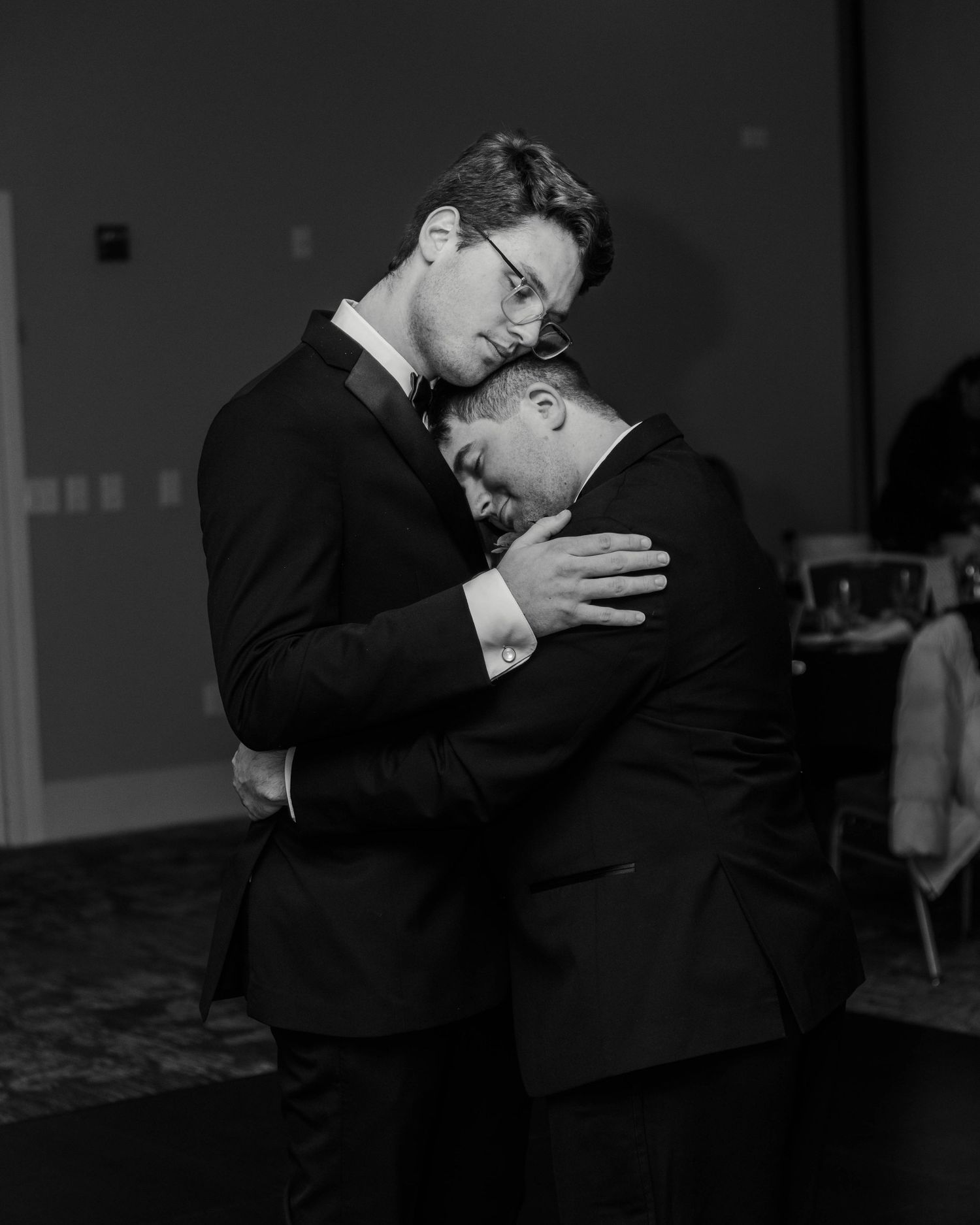 Two gay men sharing their first dance at their wedding, holding each other and their heads leaning on each other.