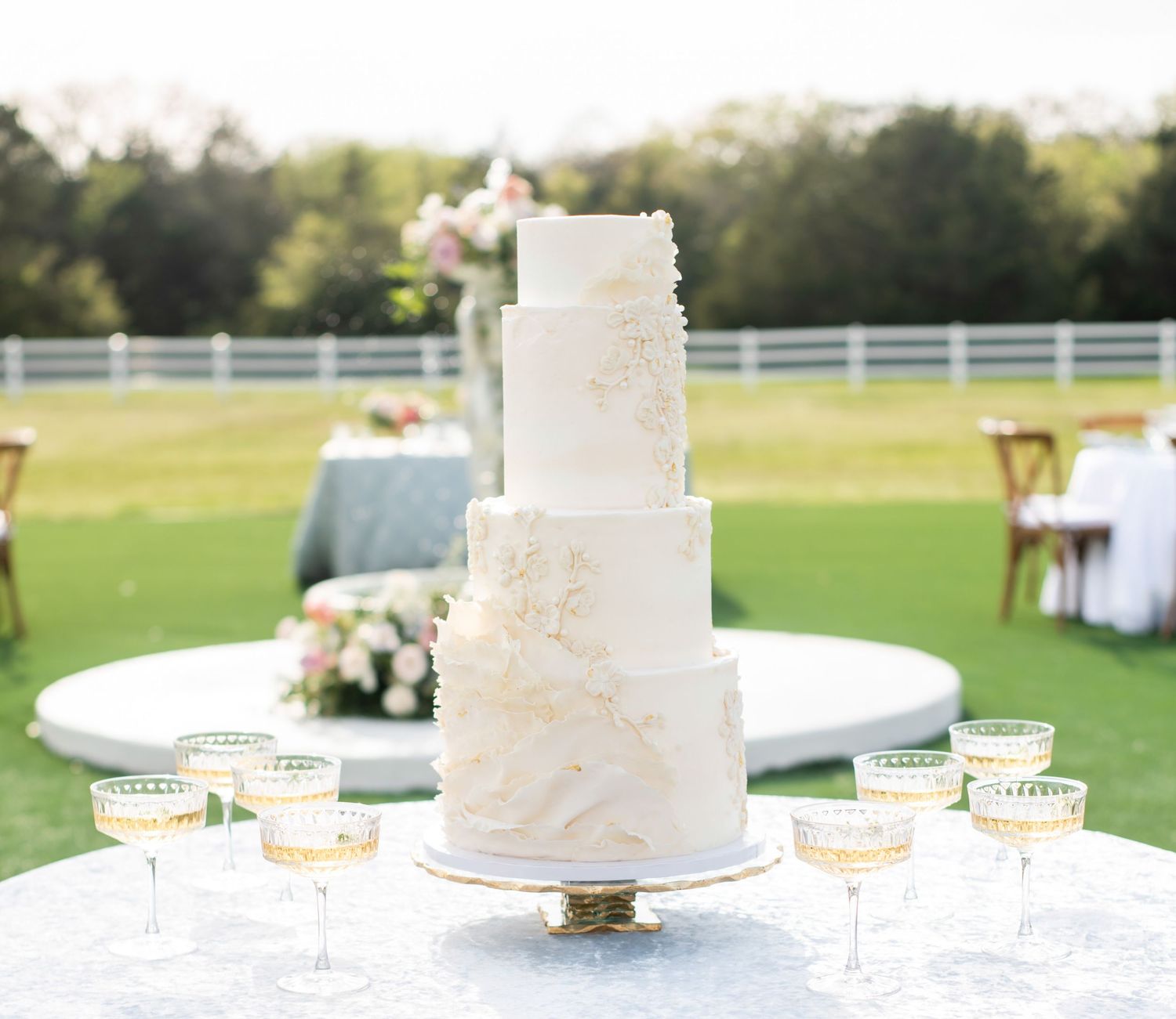 A cream colored cake that is multi-layered sits at a table with champagne glasses