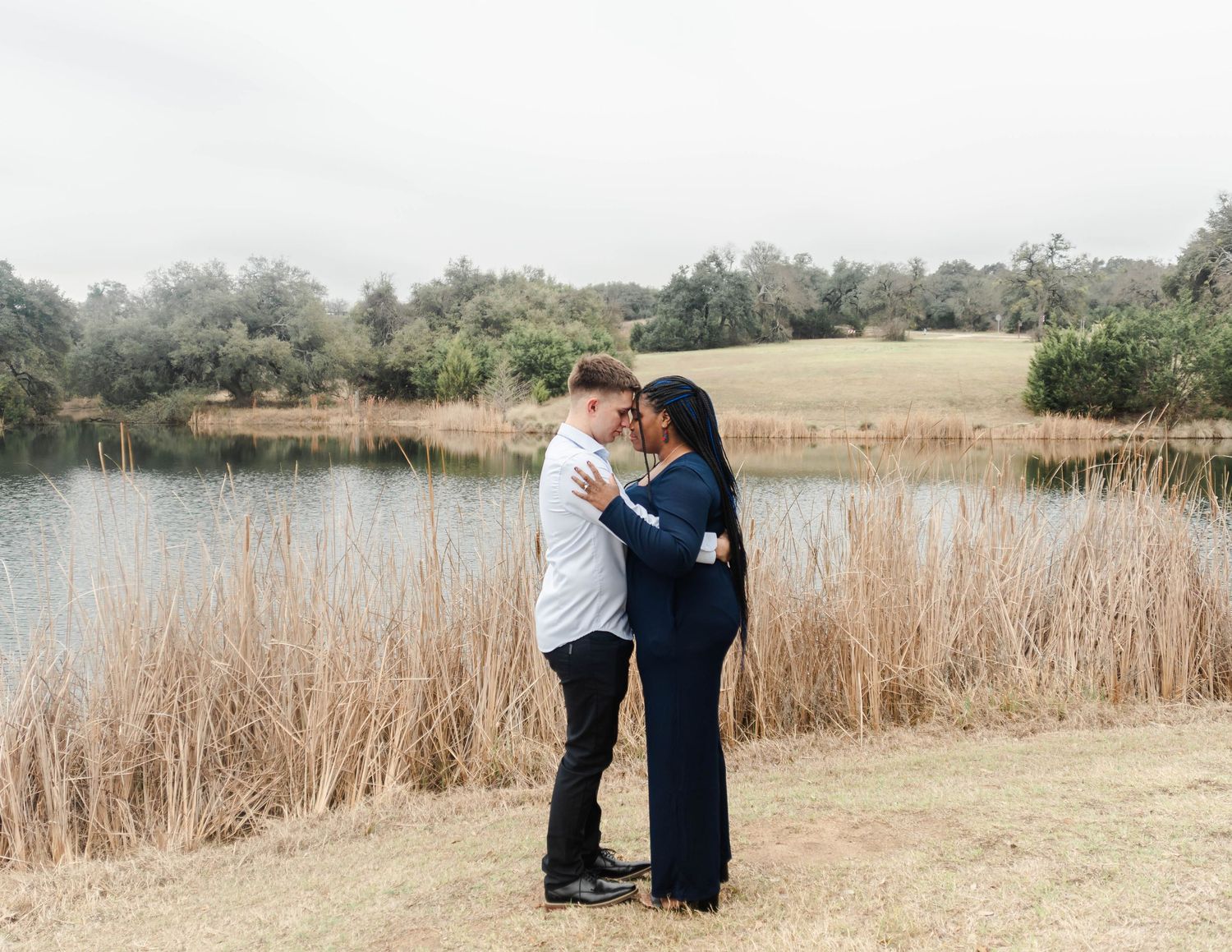 a couple posing in front of a pond with tall grass