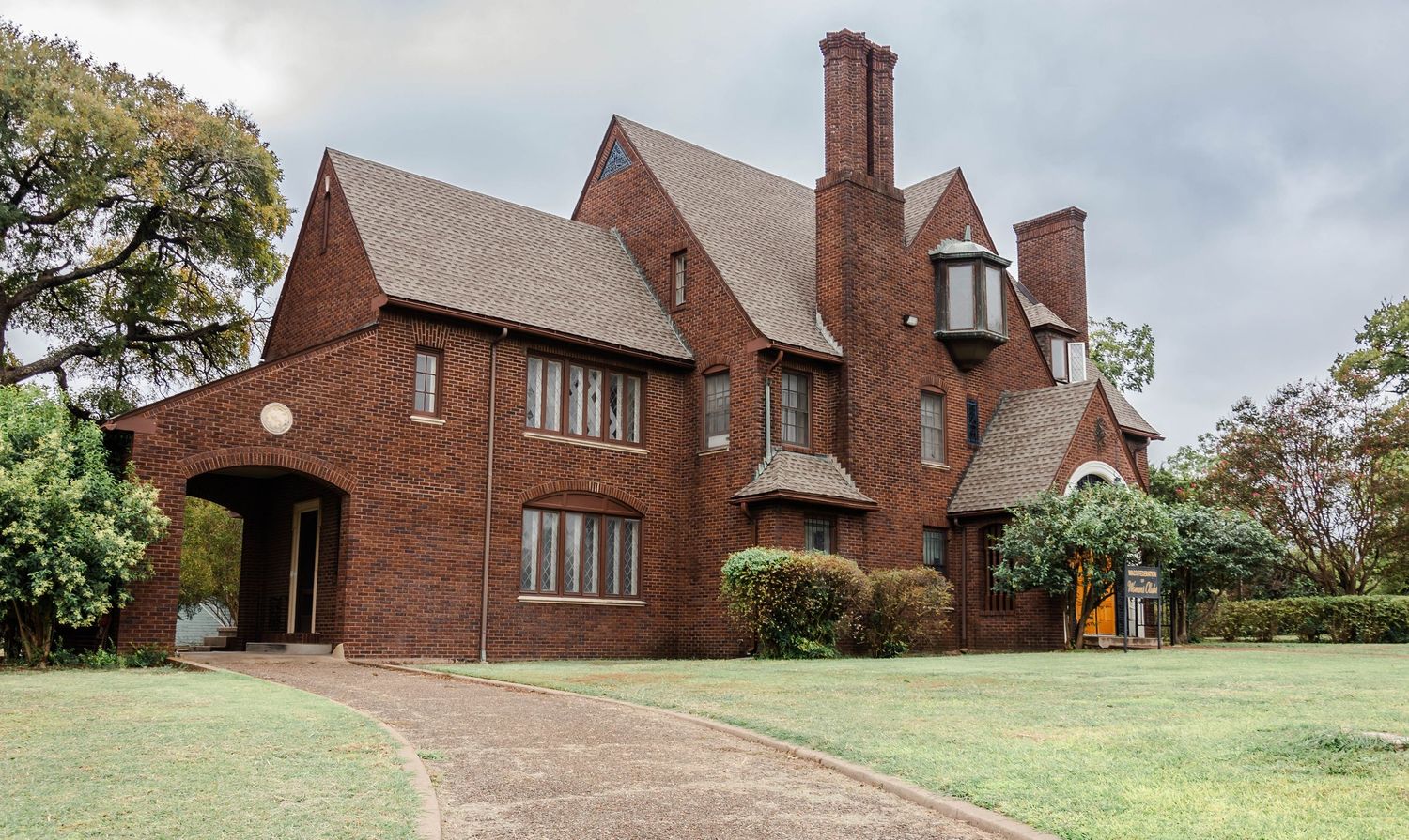 Large Tudor-style brick mansion with multiple chimneys and architectural details on spacious grounds.