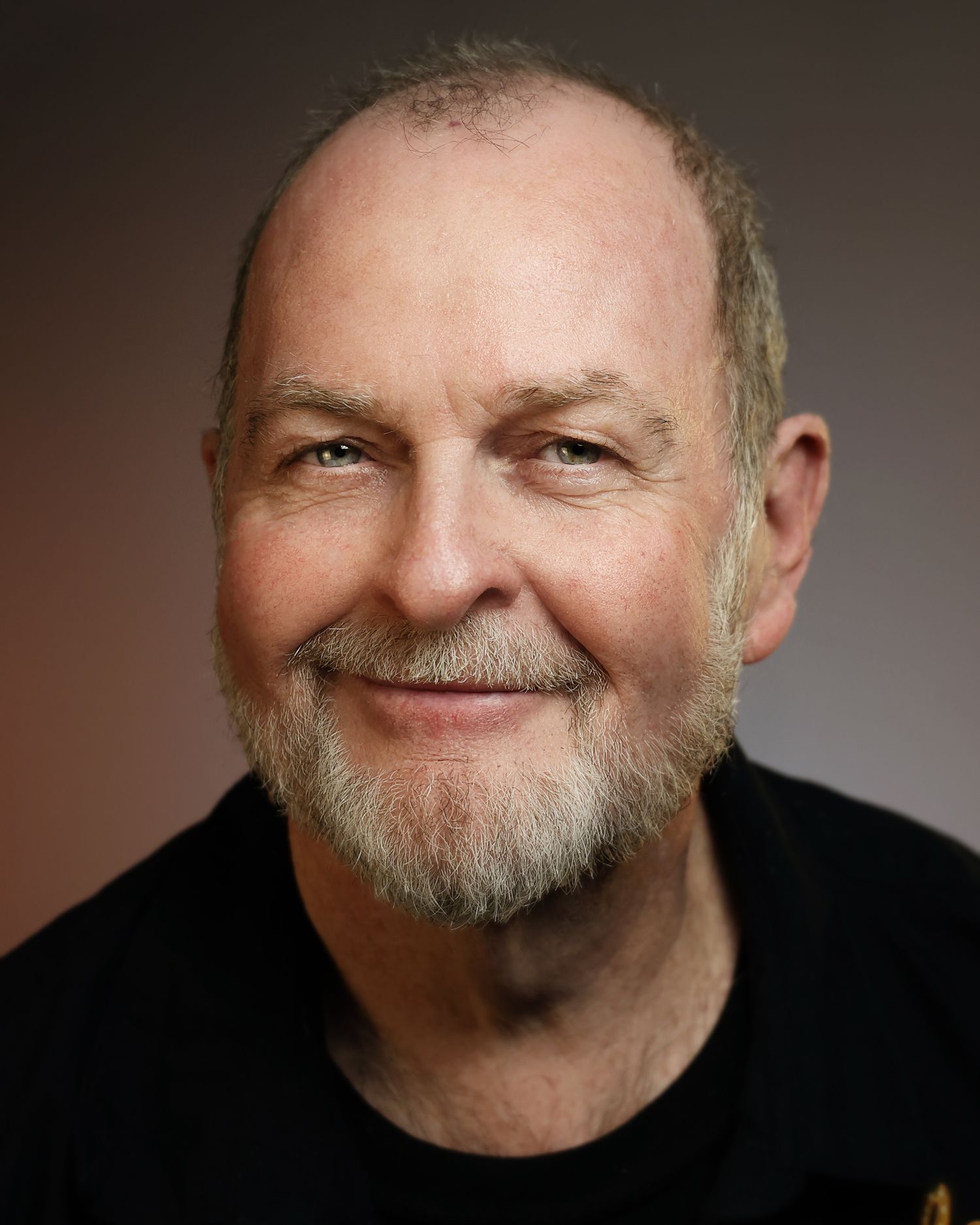 Smiling older man with gray beard and blue eyes poses for a professional headshot portrait photo.