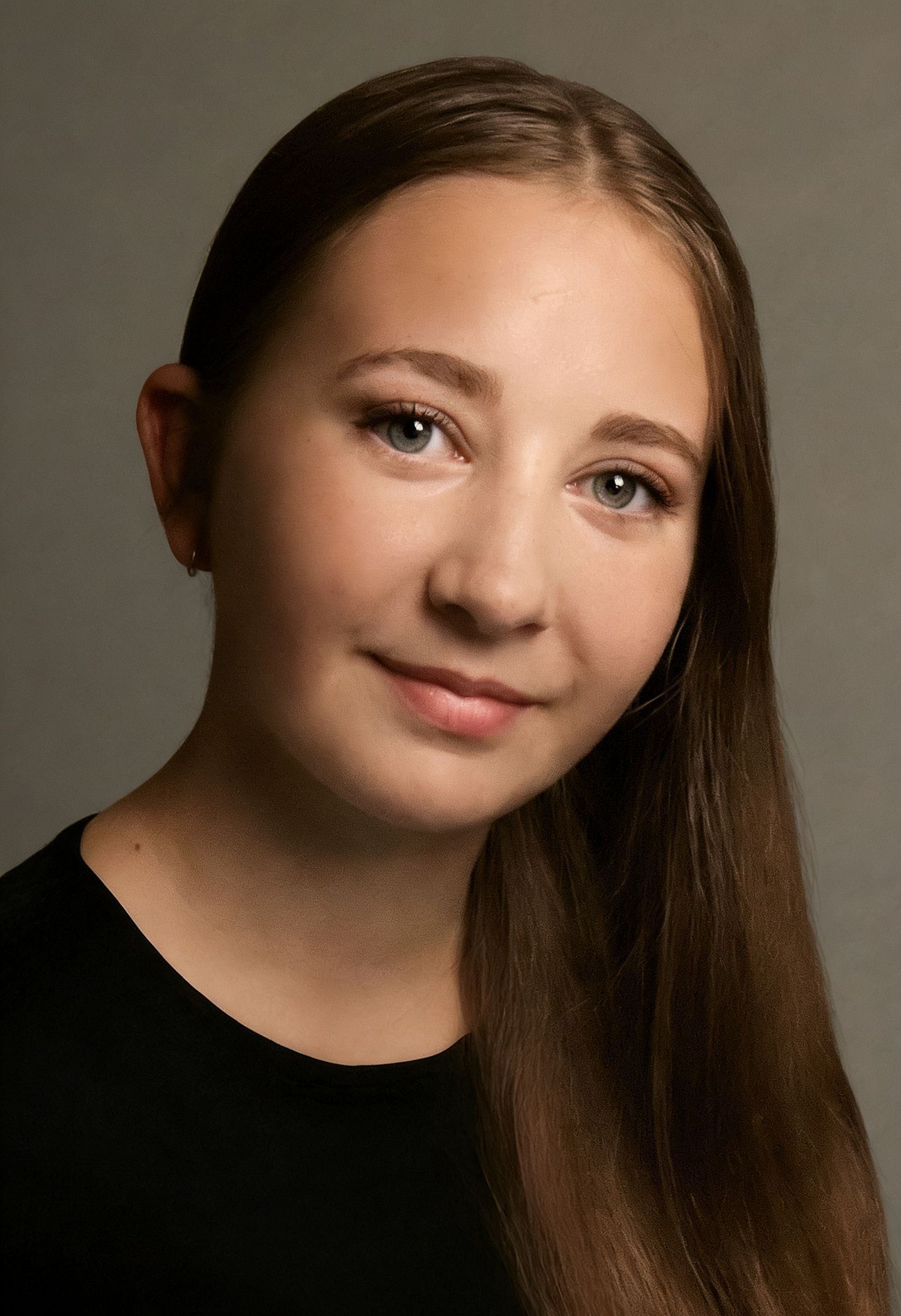 Young girl with long brown hair and blue eyes wearing a black top poses for a professional portrait photo.