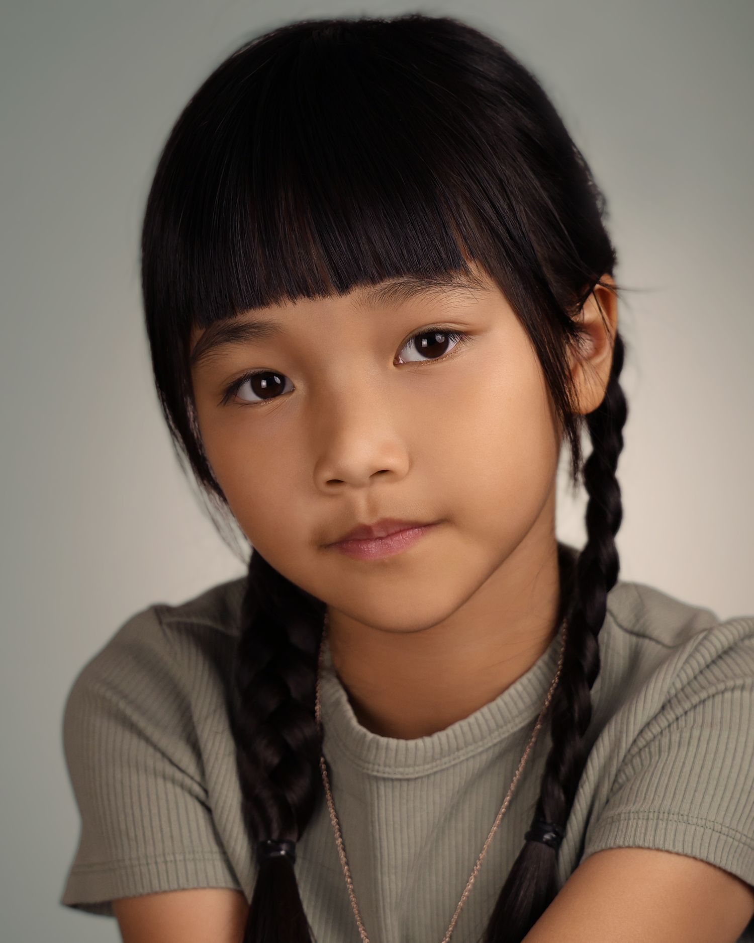 Young girl with black braided pigtails and bangs wearing a gray ribbed t-shirt, portrait photo.
