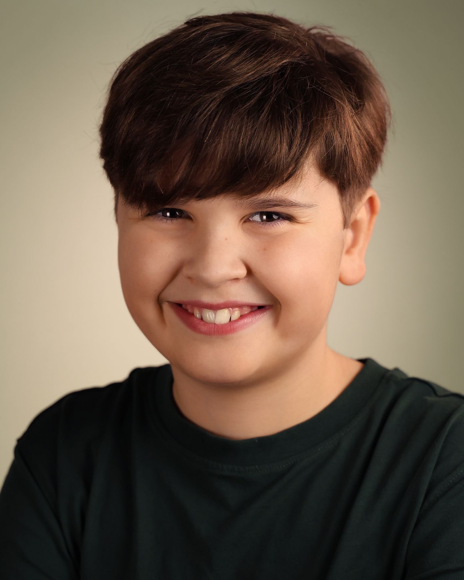 Smiling young boy with brown hair wearing a dark green shirt in a professional headshot photo.