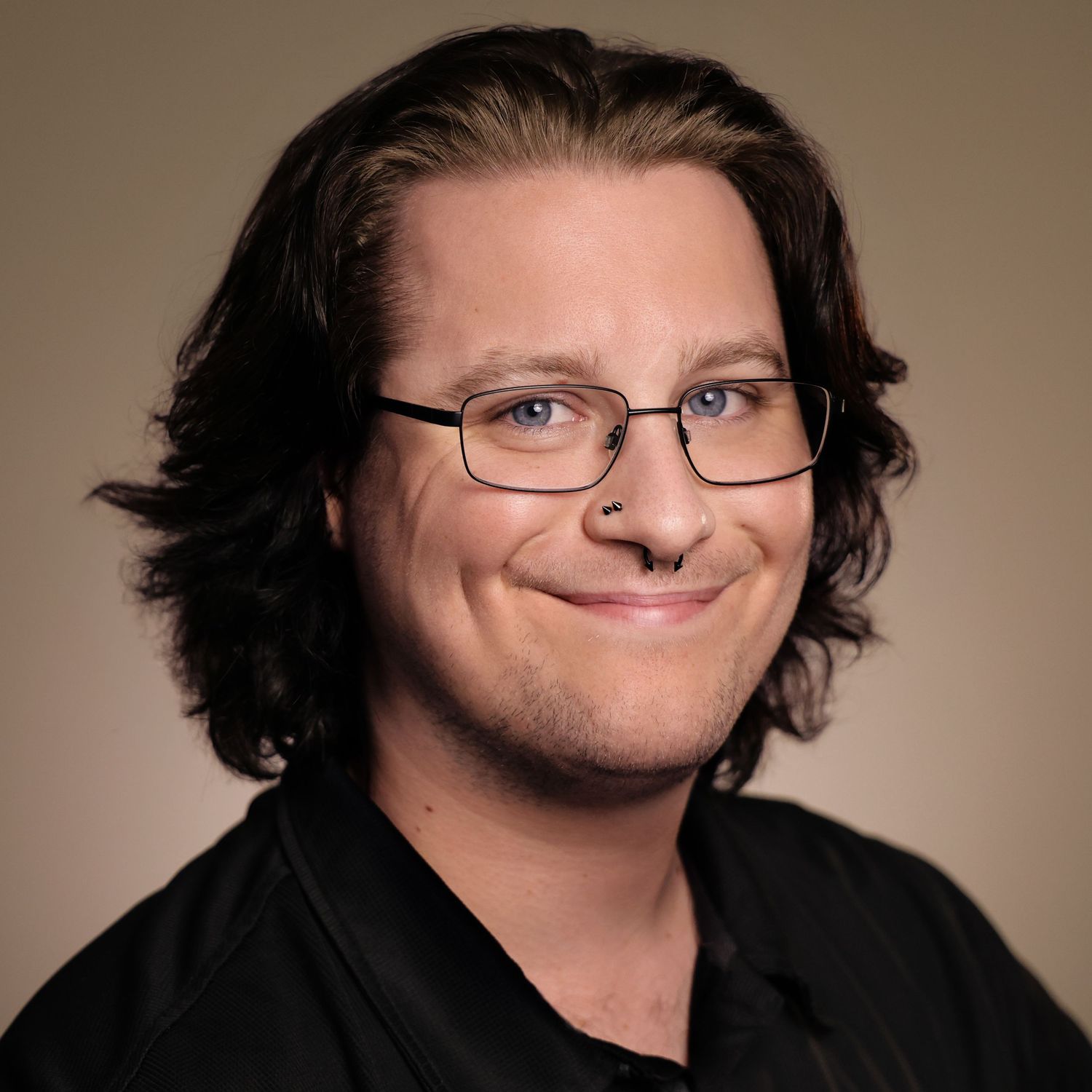 Professional headshot of a smiling man with dark hair and glasses wearing a black shirt against a neutral background.
