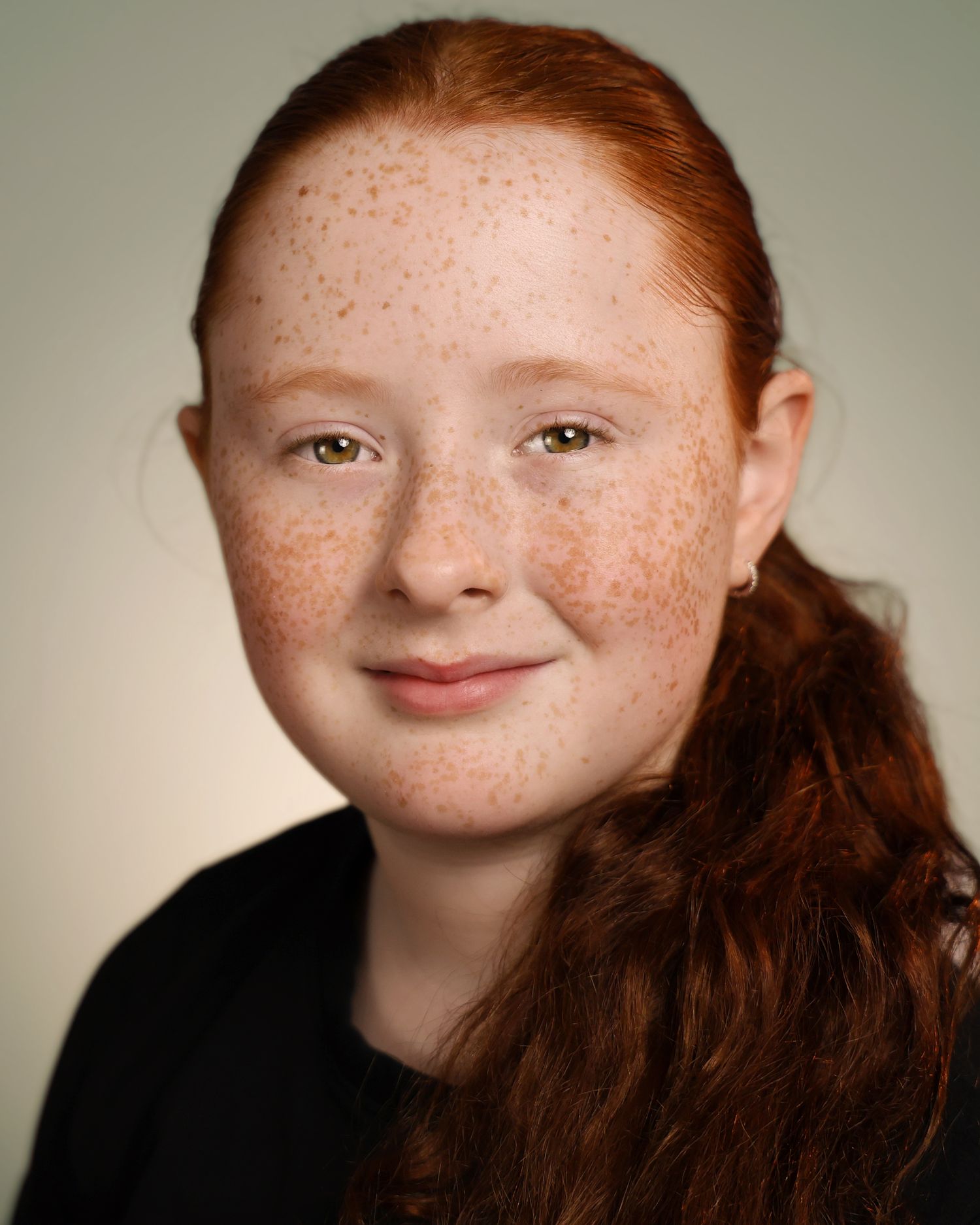 Young girl with red hair, freckles, and green eyes smiling in a professional headshot portrait.