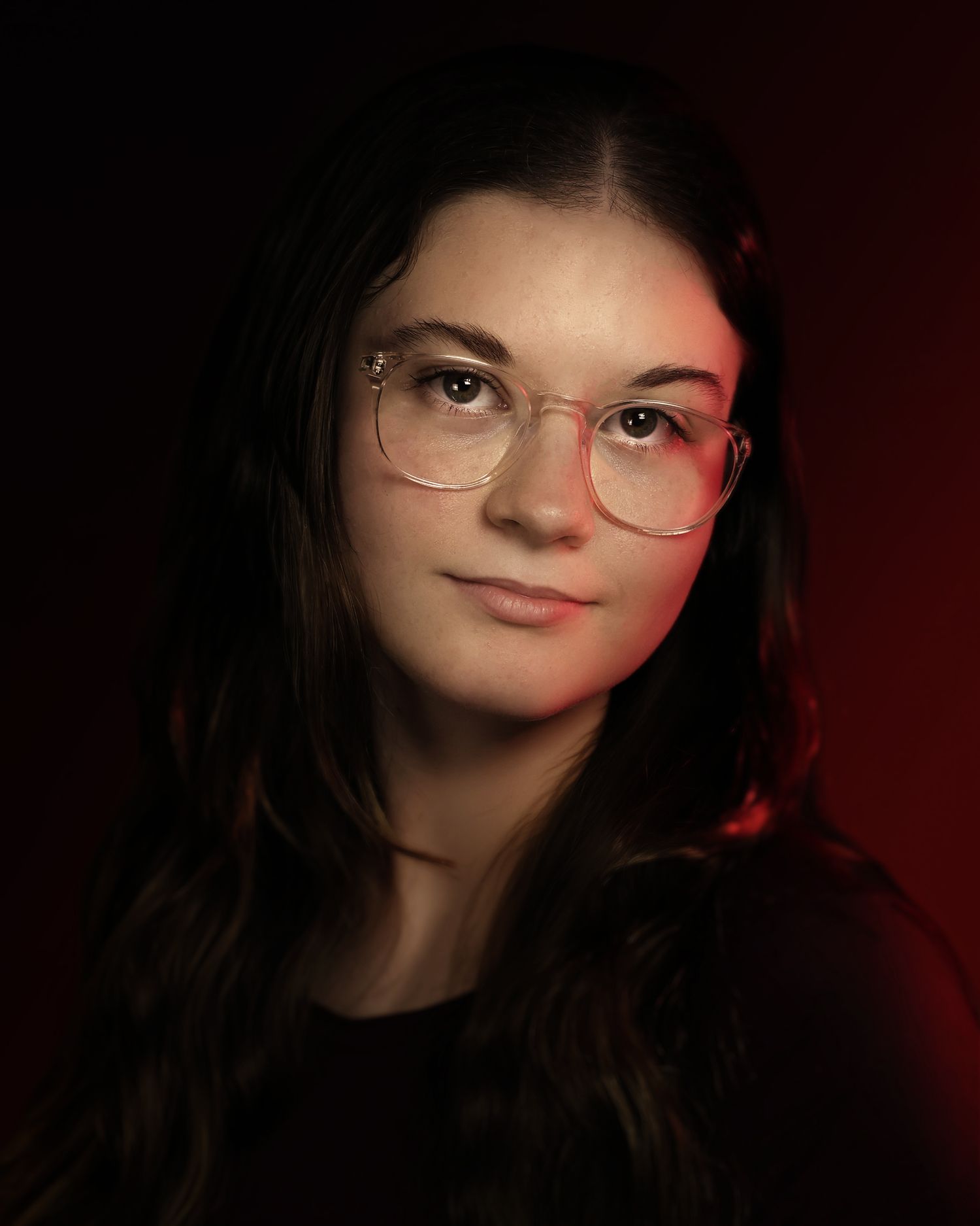 Young woman with glasses posing in dramatic red and dark studio lighting portrait photography.