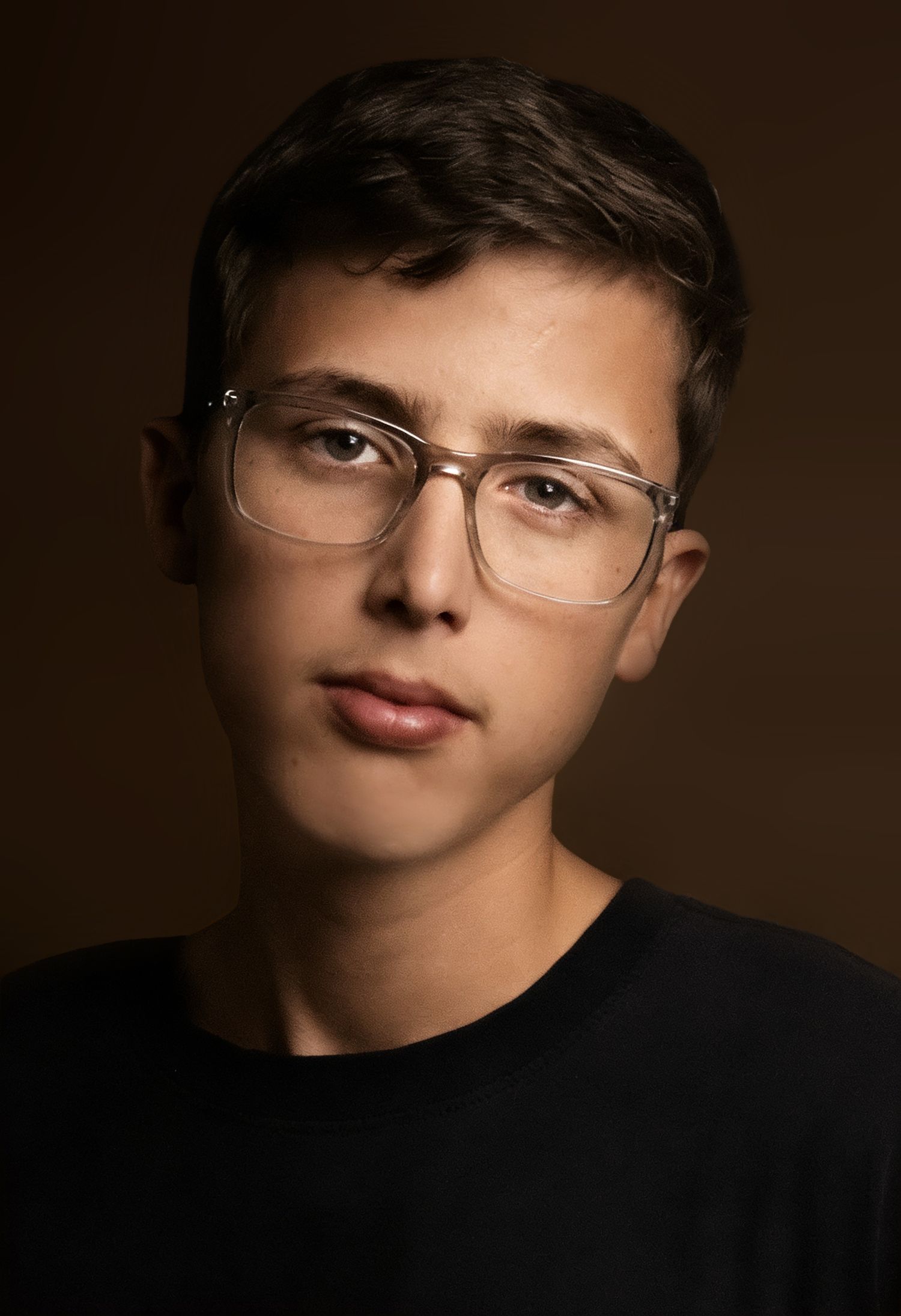 Young man with short brown hair wearing clear-framed glasses and a black t-shirt against a dark background.