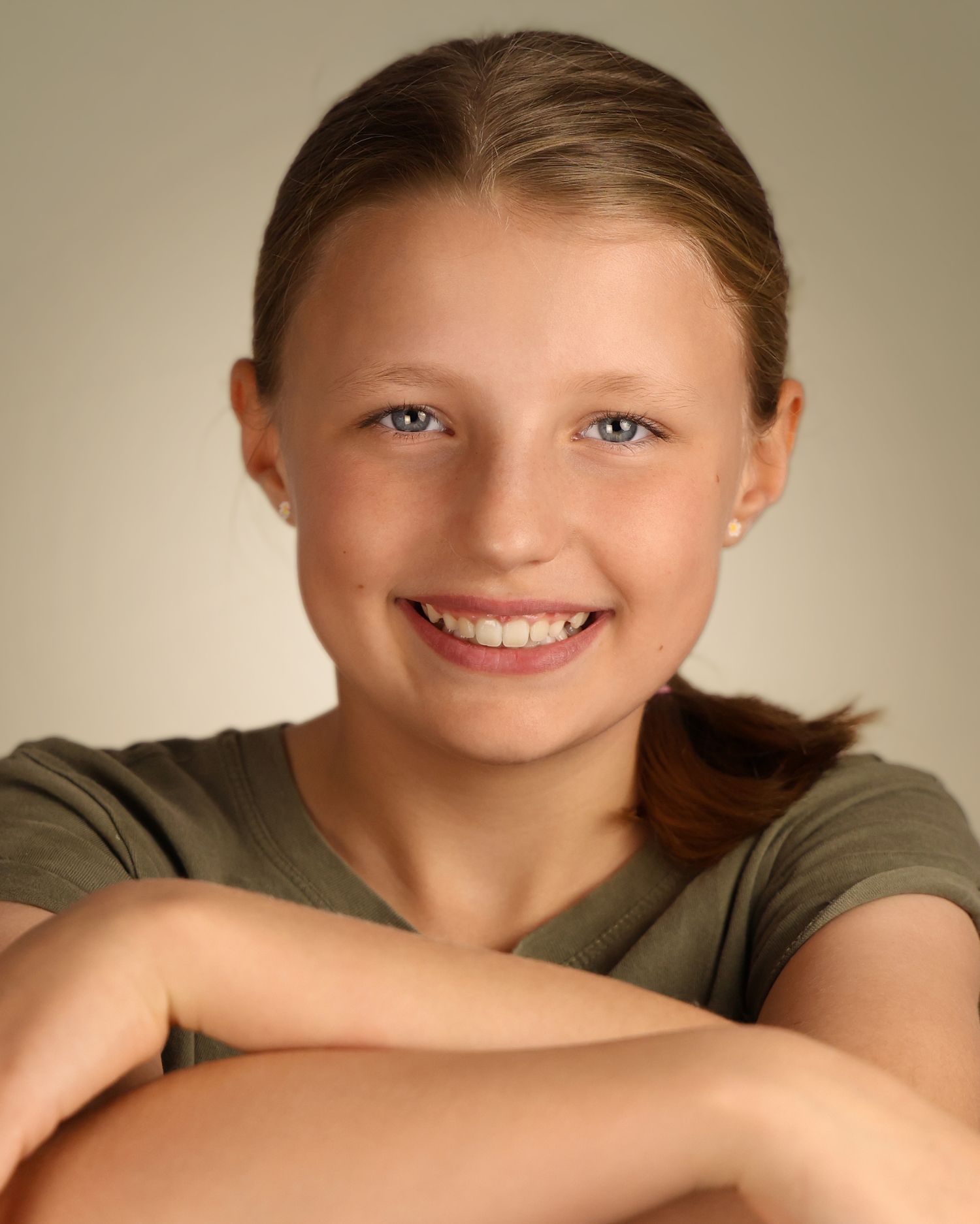 Smiling young girl with blue eyes, brown hair in a ponytail, wearing a green shirt, posing for a portrait photo.