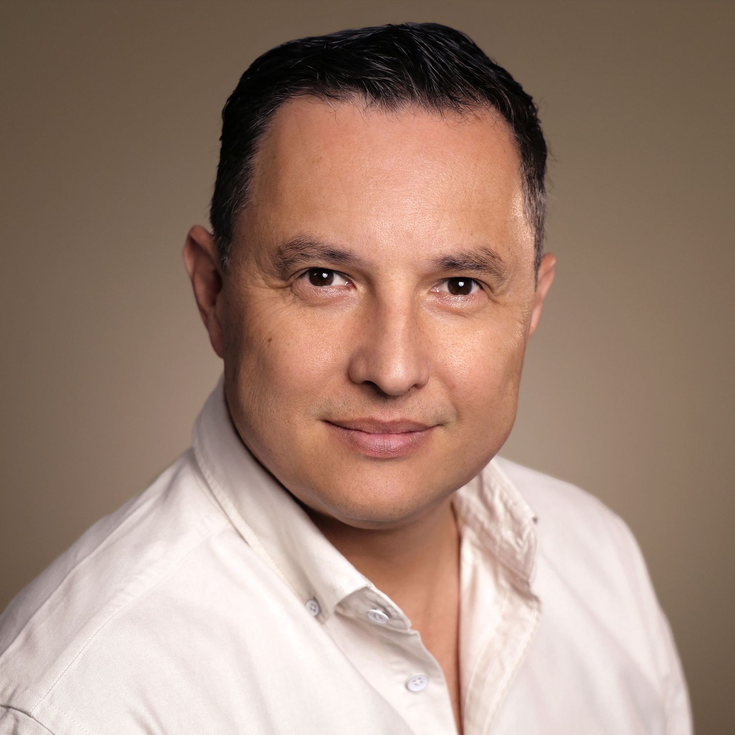 Professional headshot of a confident middle-aged man in a white shirt against a neutral beige background.