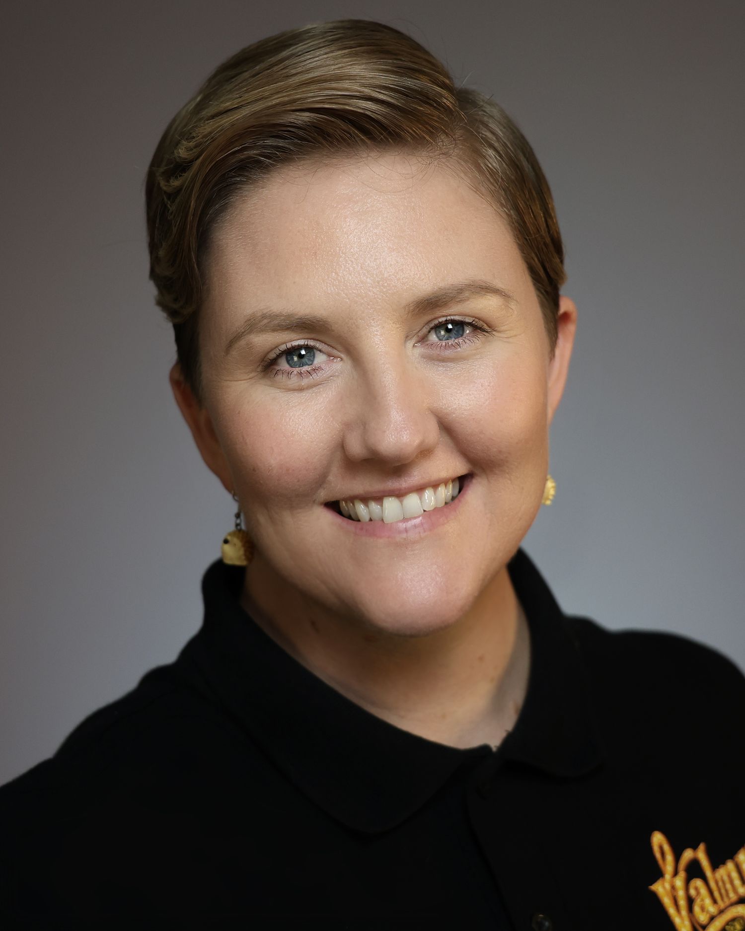 Professional headshot of a smiling woman with short blonde hair wearing a black Valpo polo shirt.