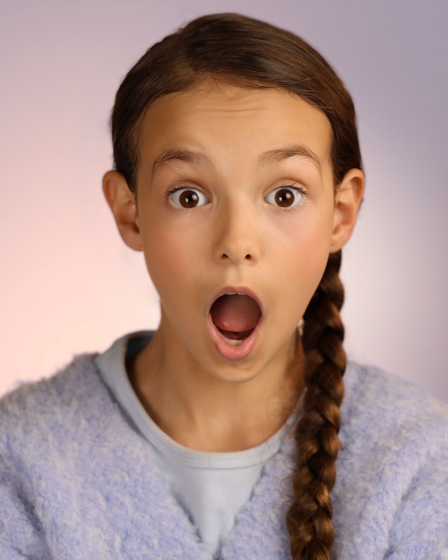 A surprised young girl with a brown braid, wearing a blue sweater, making an astonished face against a purple background.