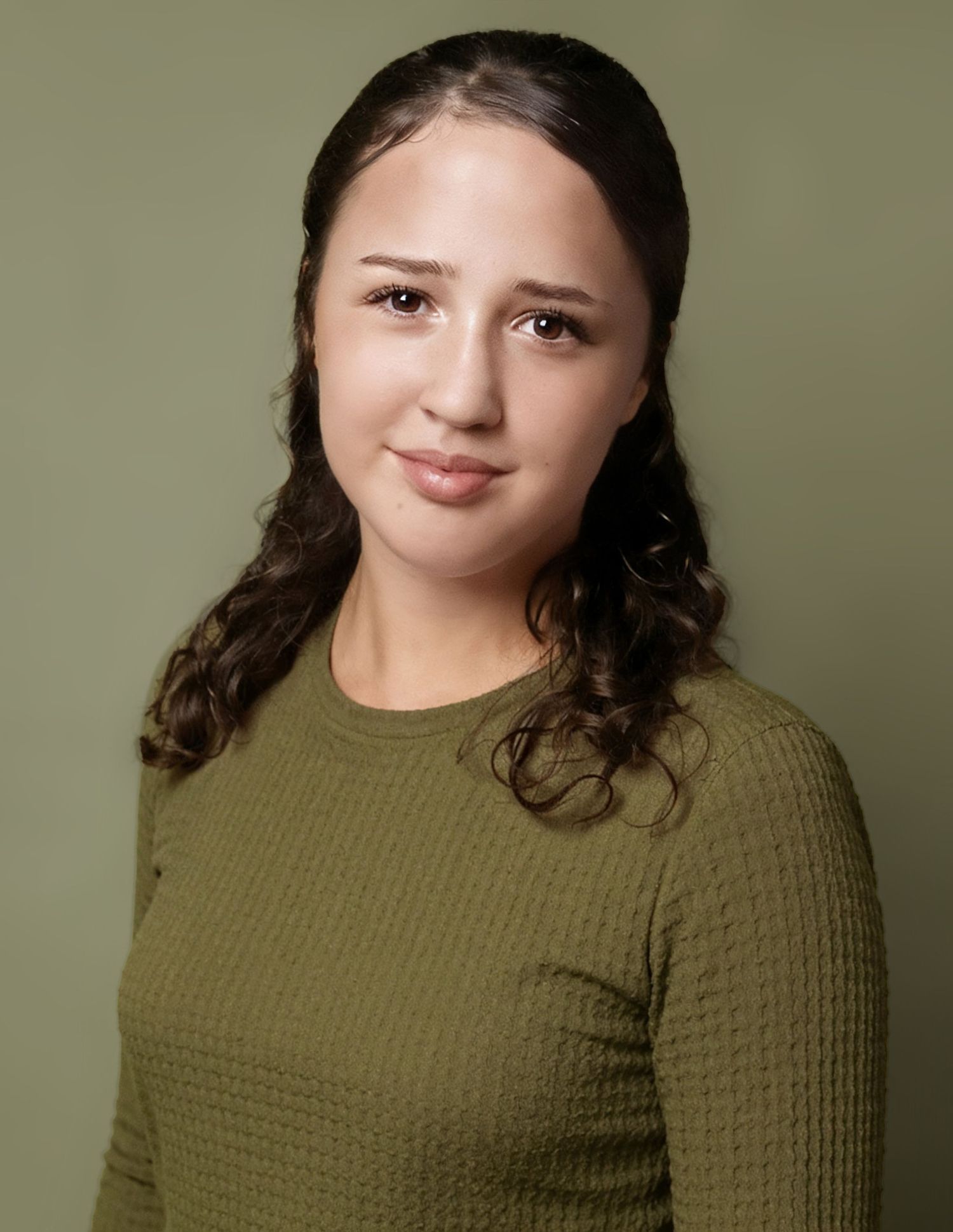 Young woman with curly dark hair in olive green waffle-knit sweater poses for professional headshot photo.