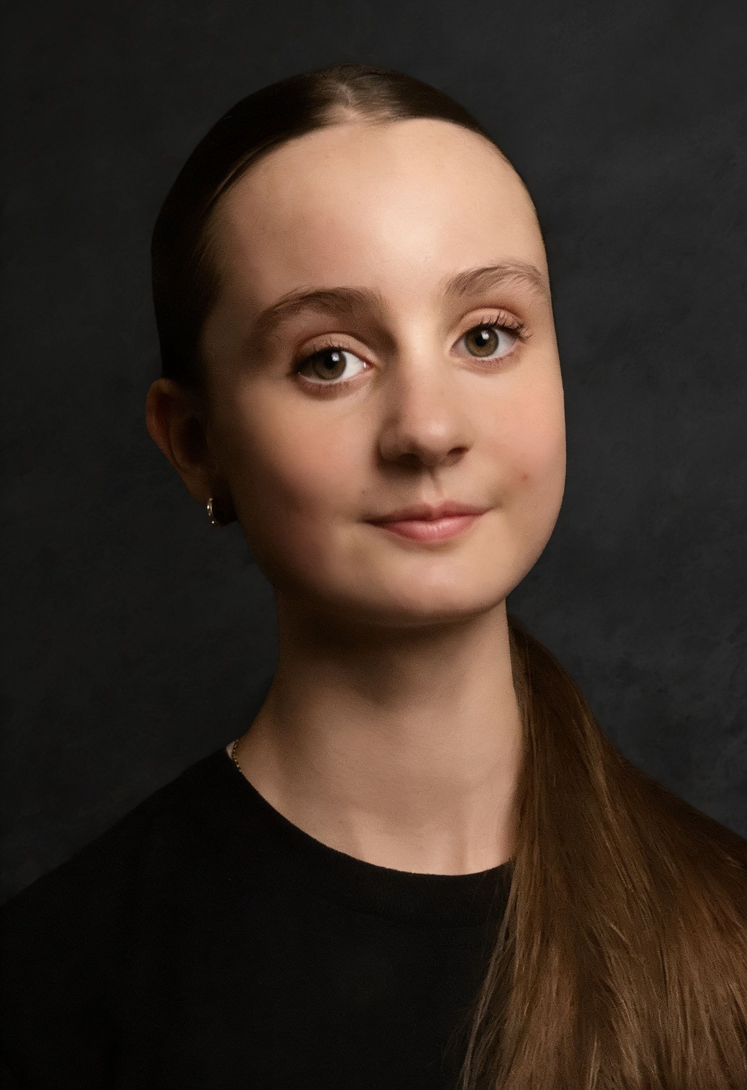 Young woman with brown hair in a ponytail, wearing a black top, posing for a professional portrait photo.
