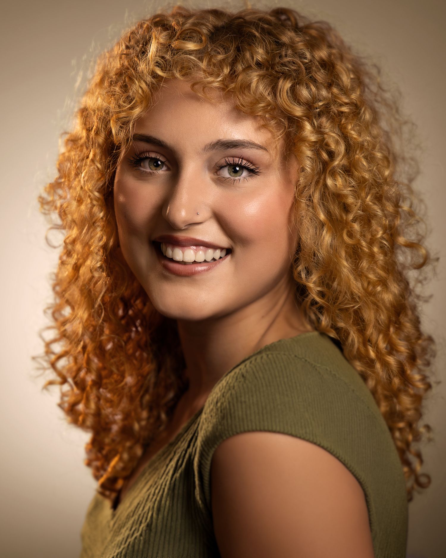 Young woman with voluminous curly auburn hair smiling warmly in a professional headshot portrait.