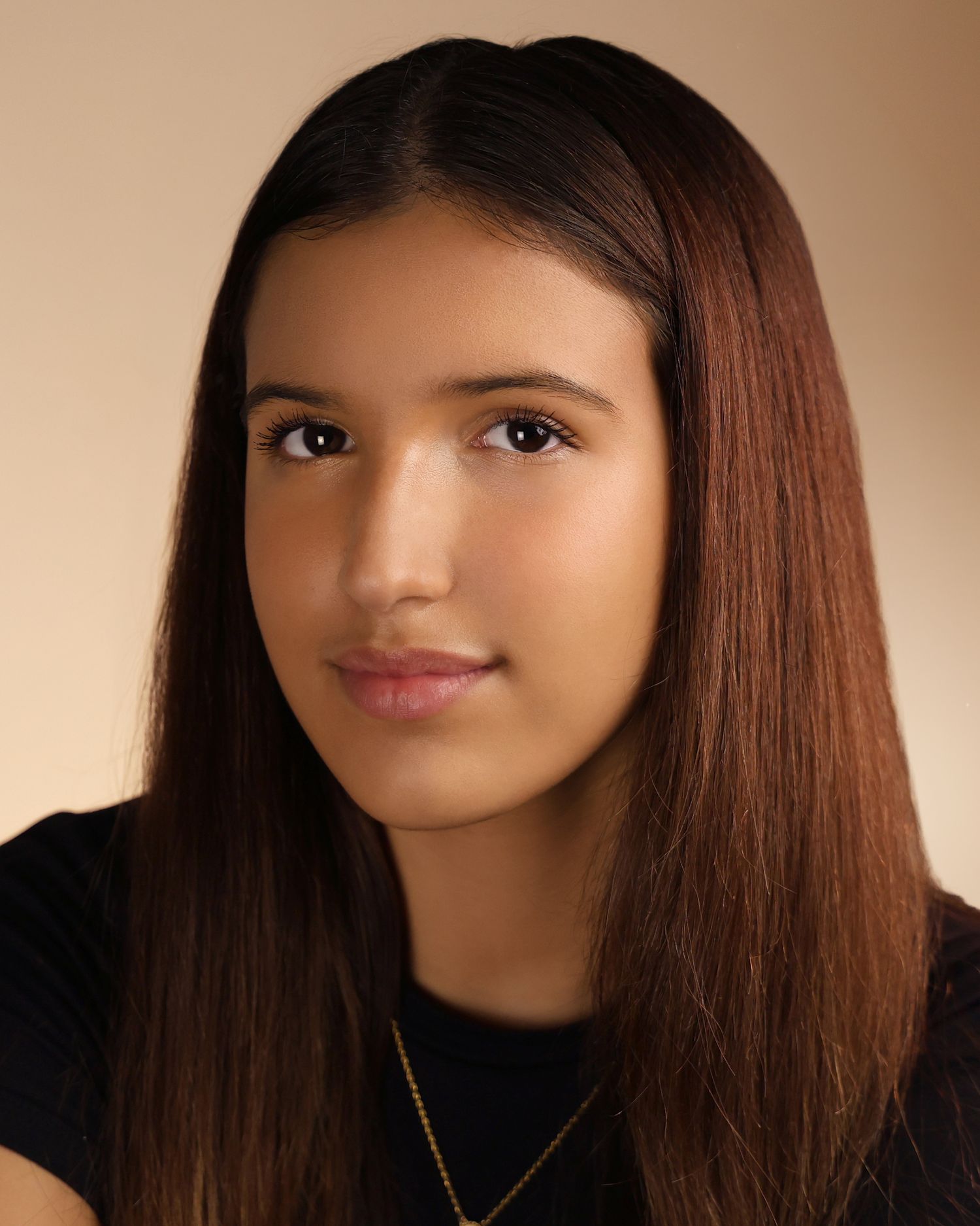 Young teenage girl with long straight auburn hair and a gold necklace poses for a professional headshot portrait.