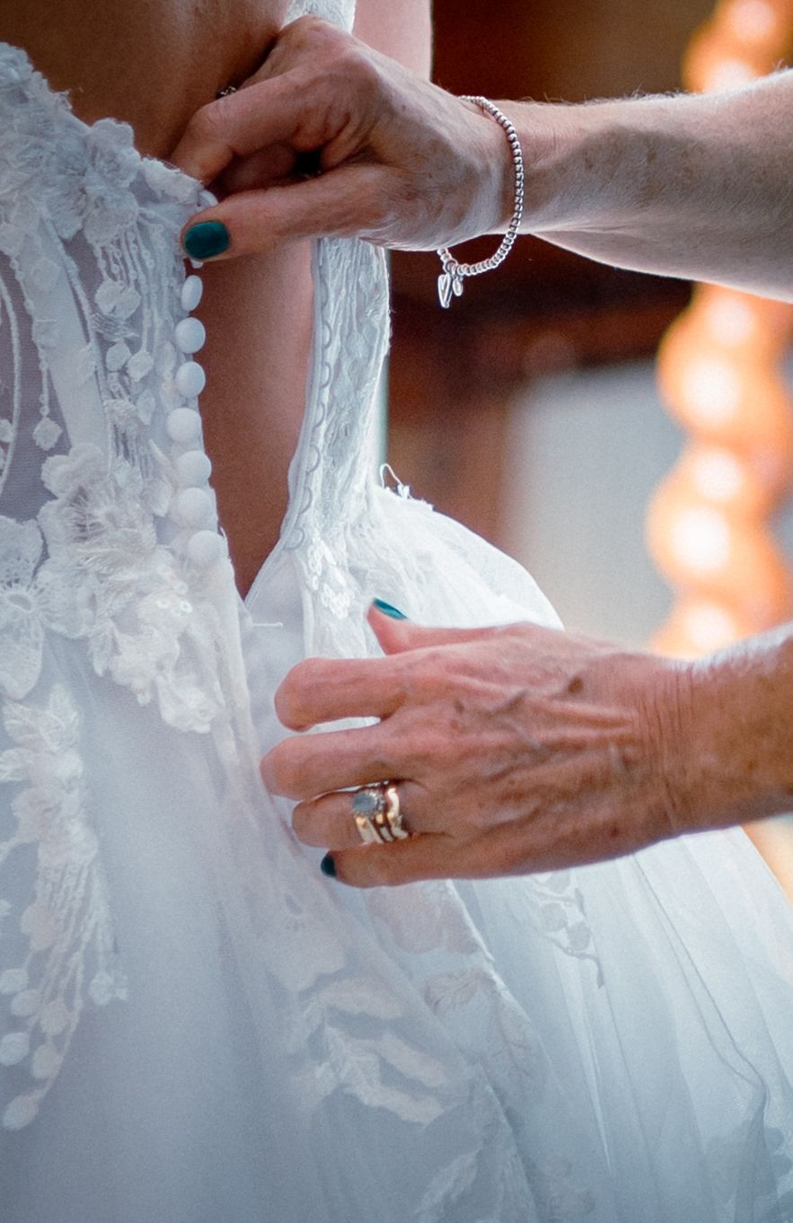 Close-up of hands carefully fastening delicate lace buttons on back of elegant bridal wedding gown.