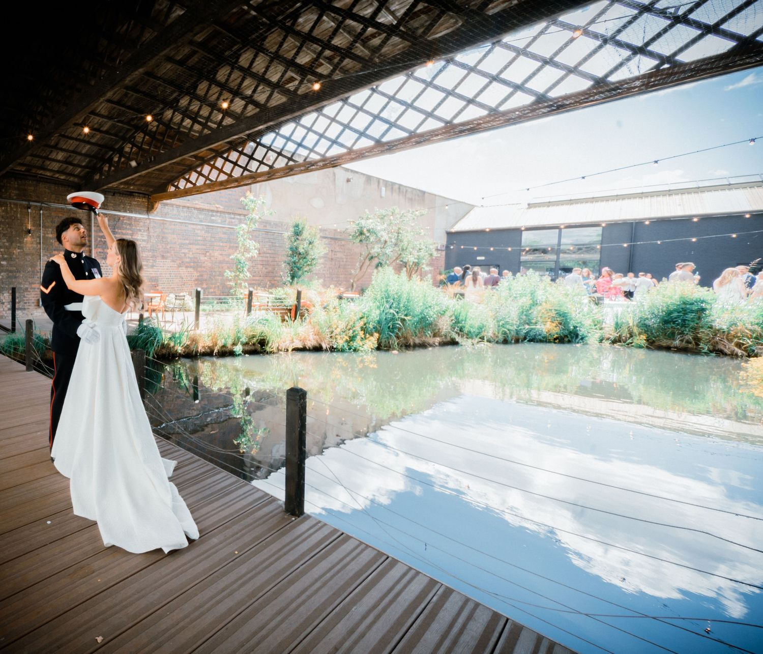 Bride and groom share first dance on wooden deck overlooking a serene pond at an elegant outdoor wedding venue.