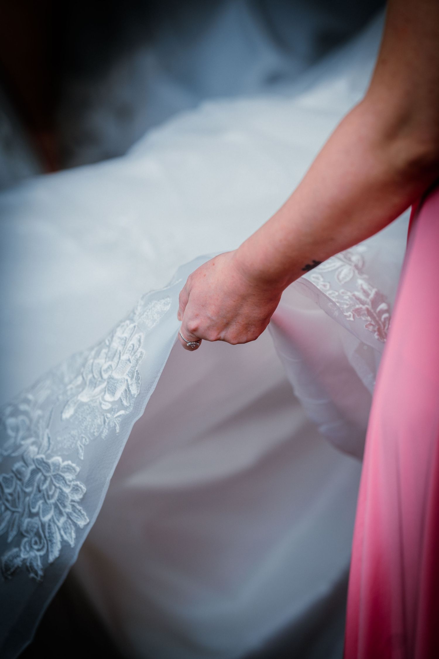 Close-up of a hand holding the delicate lace detail of a bridal wedding gown.