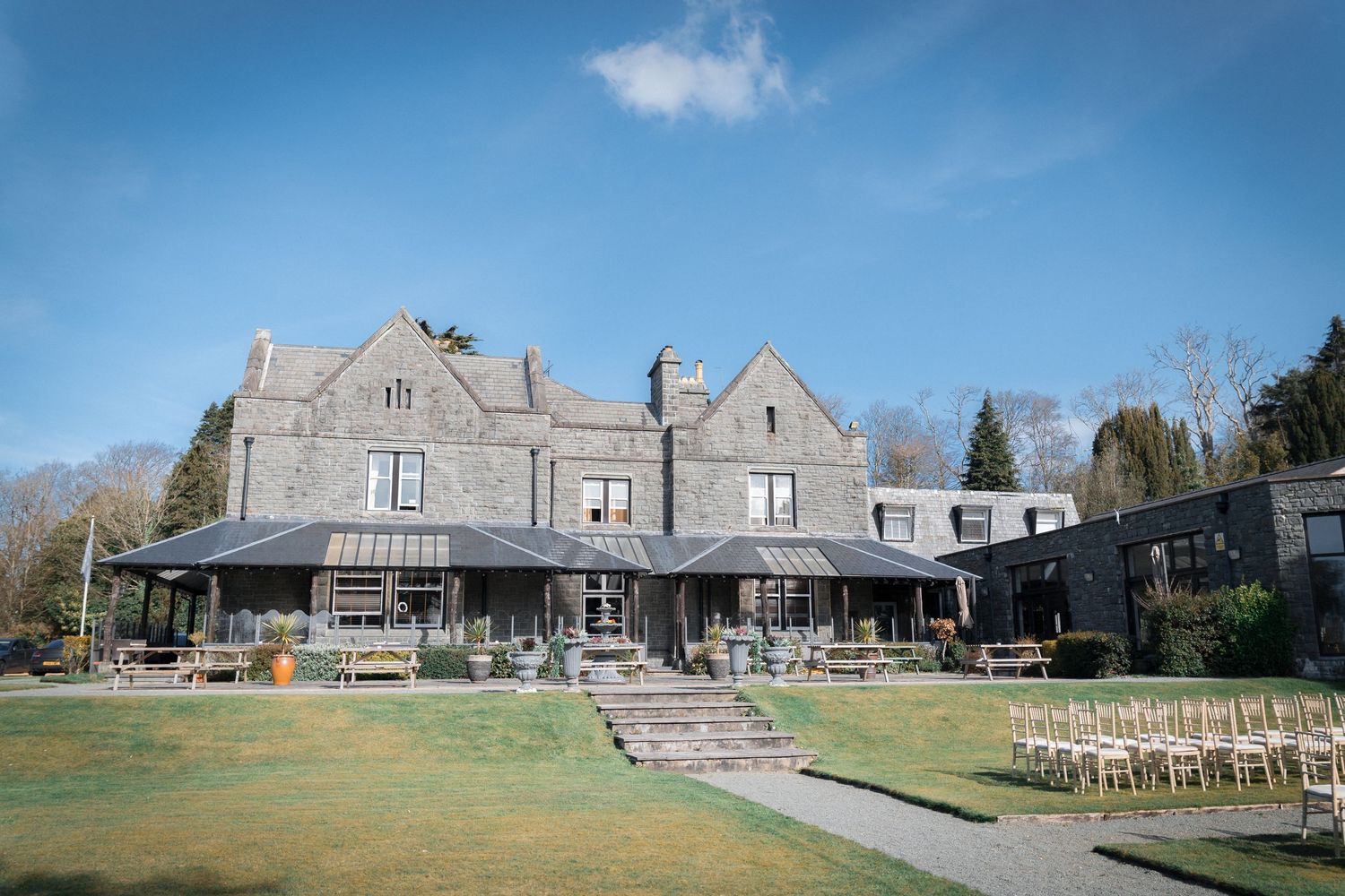 Stone manor wedding venue with manicured lawn and white chairs set up for an outdoor ceremony under blue skies.