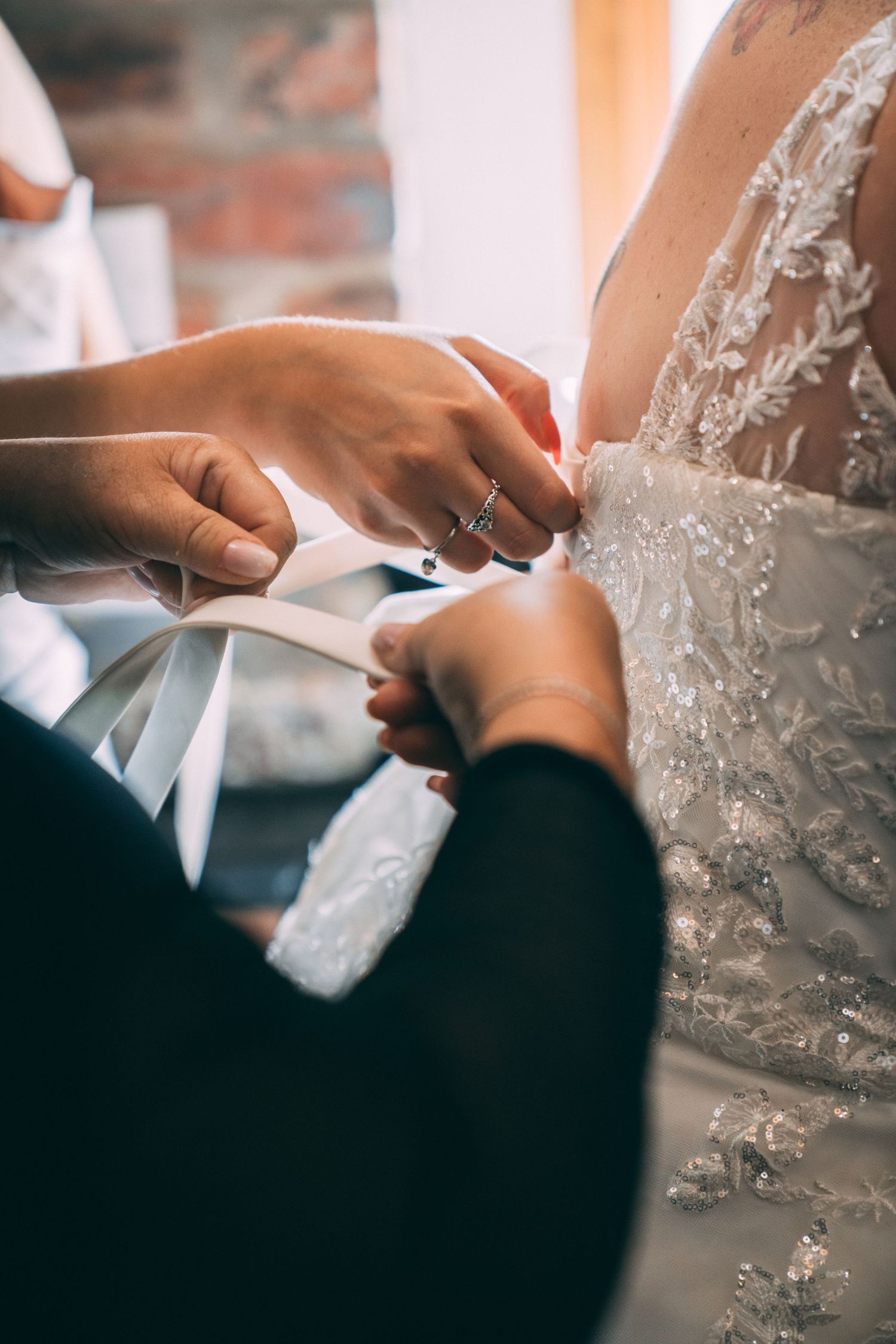Close-up of hands tying a satin ribbon bow on the back of a beaded lace wedding dress.