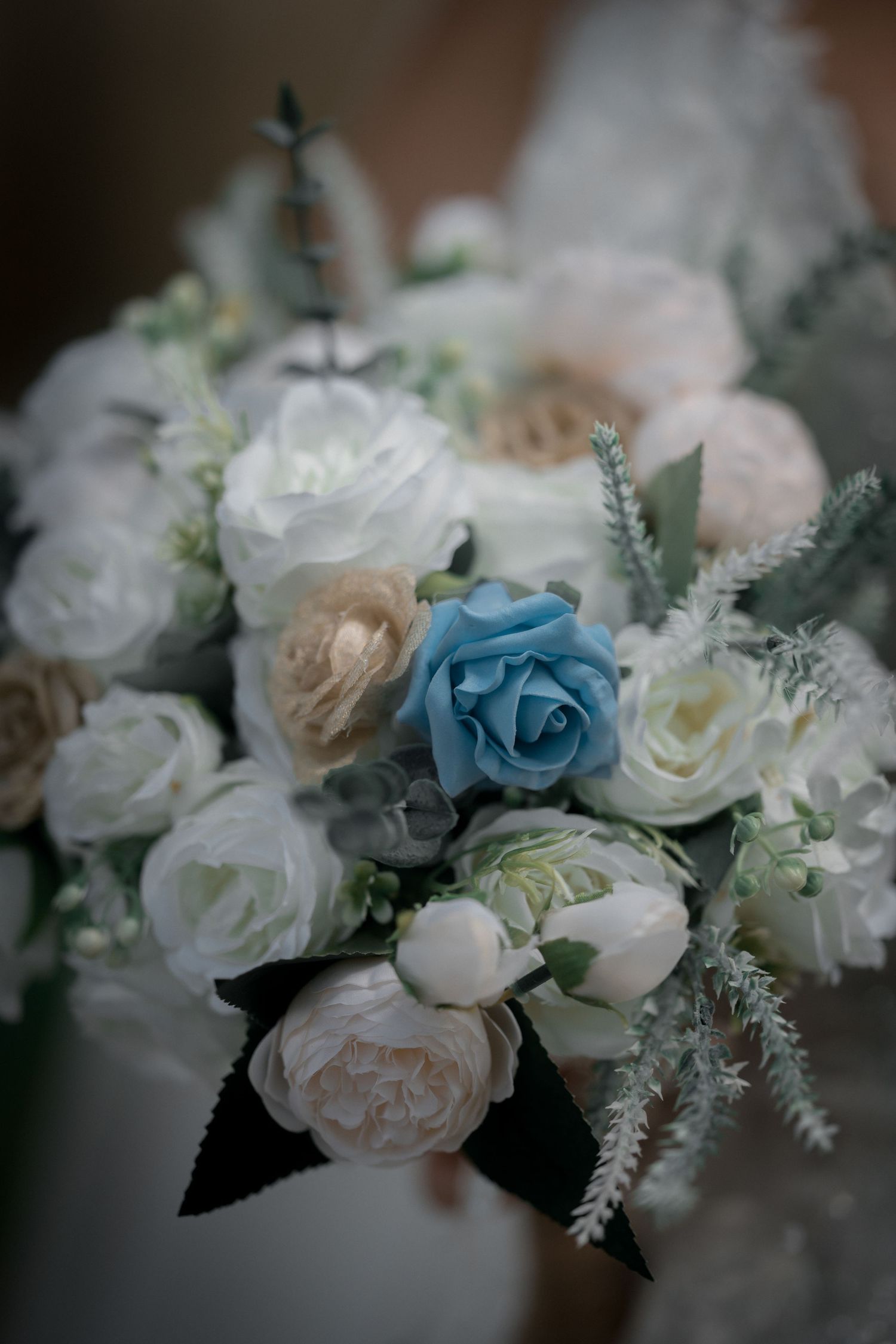 Beautiful bridal bouquet featuring white and cream roses with a single blue rose and dark ribbon accent.