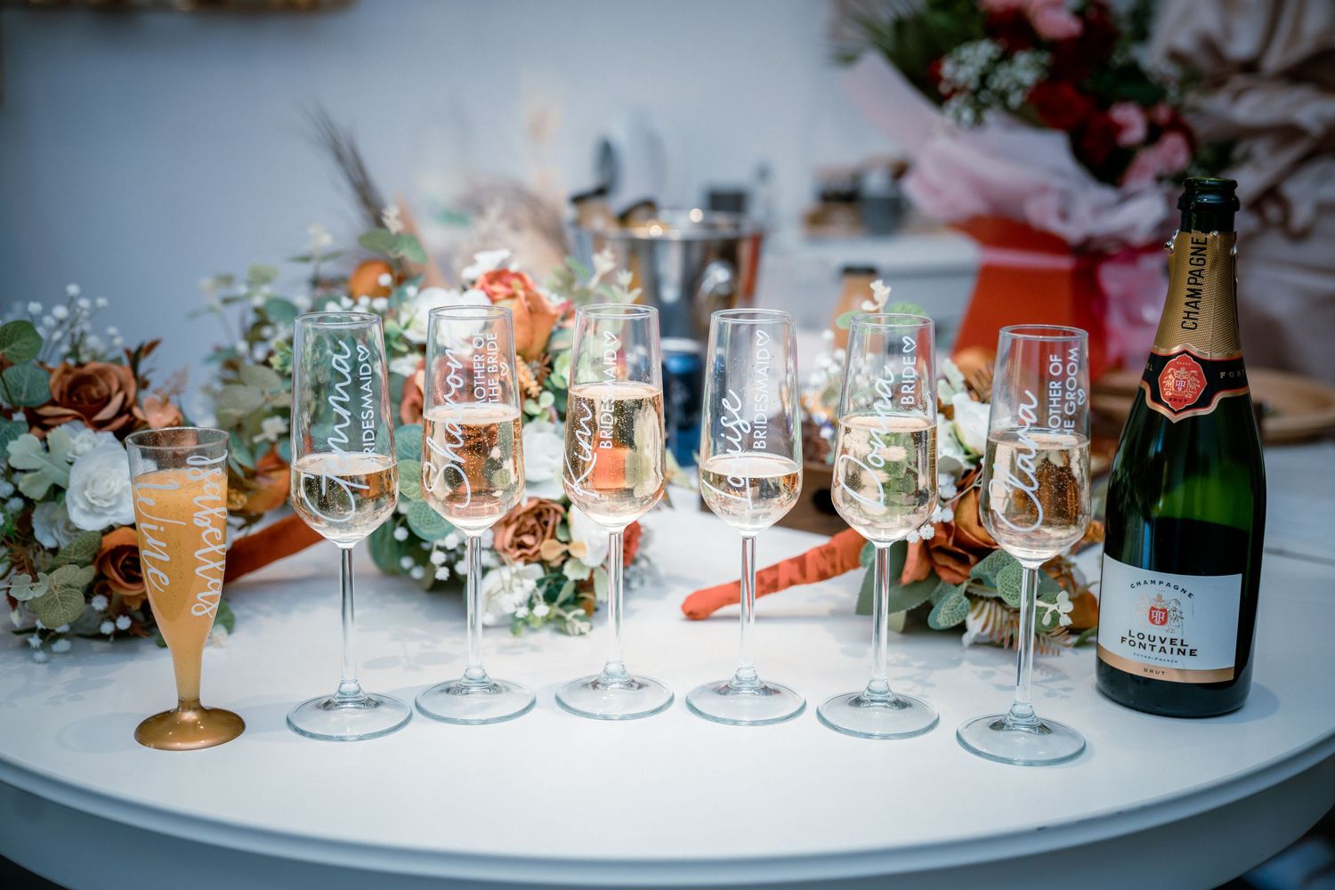 Elegant wedding champagne glasses arranged on a white table with floral decorations and a champagne bottle.
