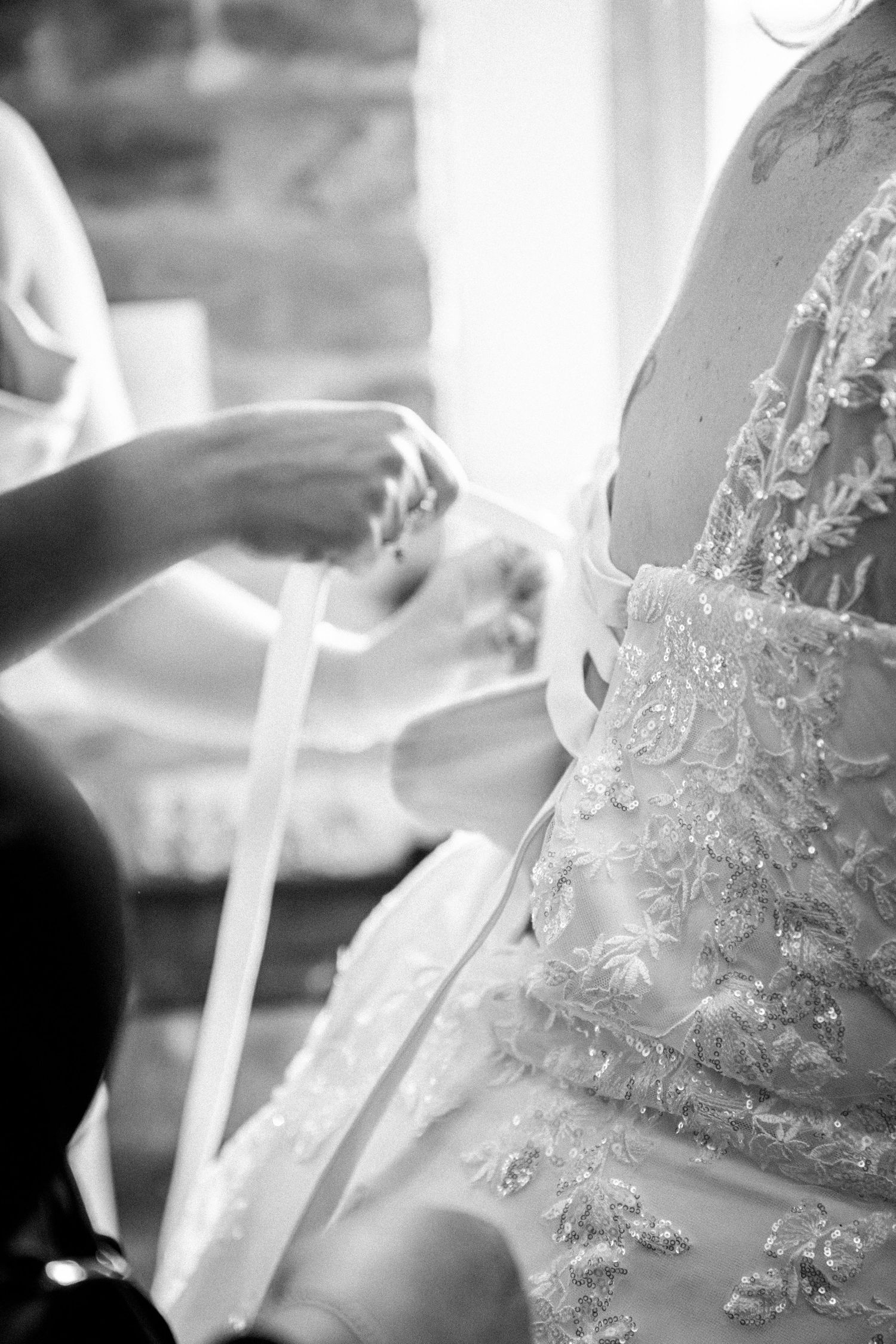 Black and white close-up of hands fastening the ribbon detail on an embellished bridal gown.