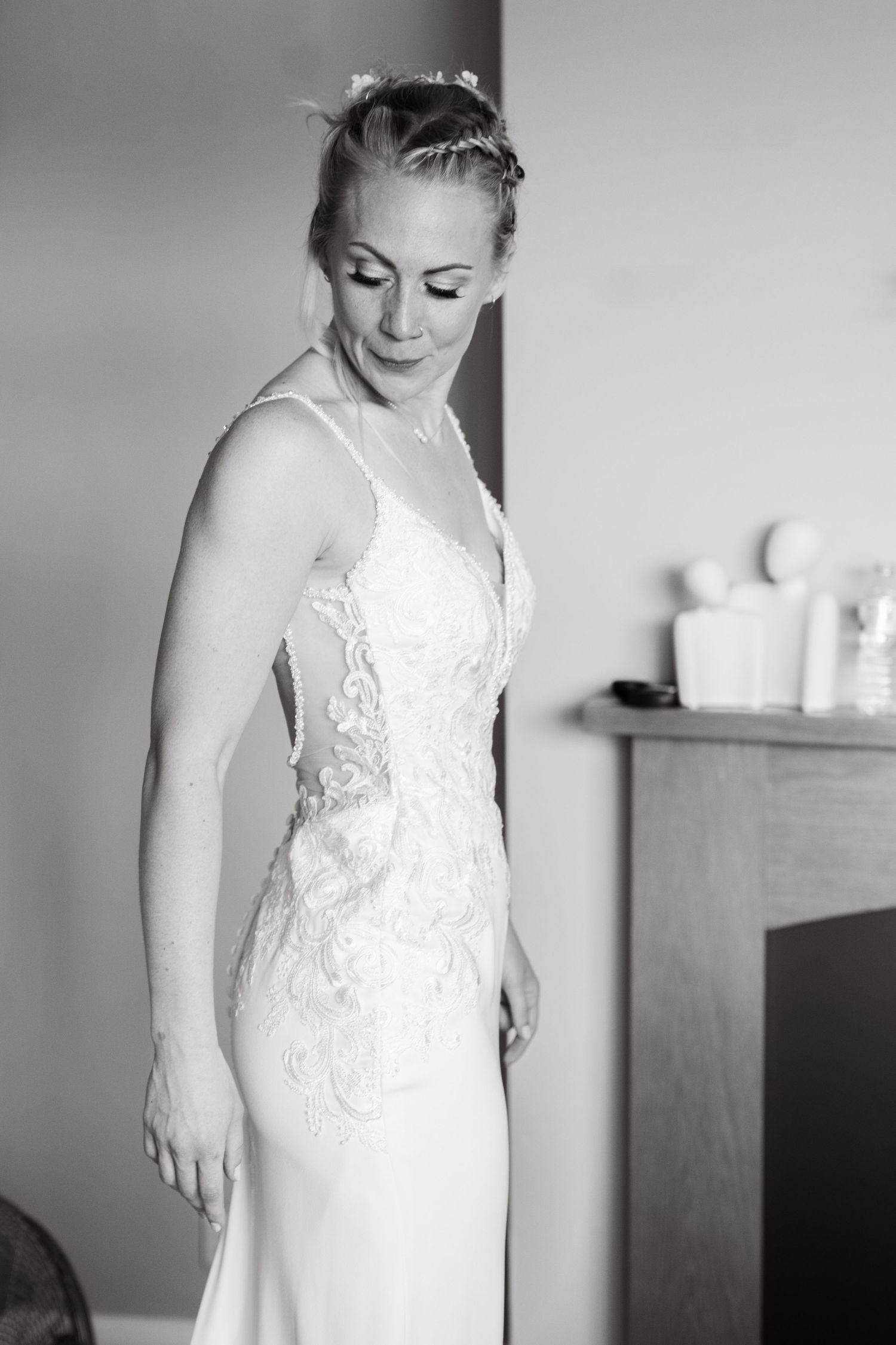 Elegant bride in a sleeveless lace wedding gown with floral hair accessory in black and white portrait.