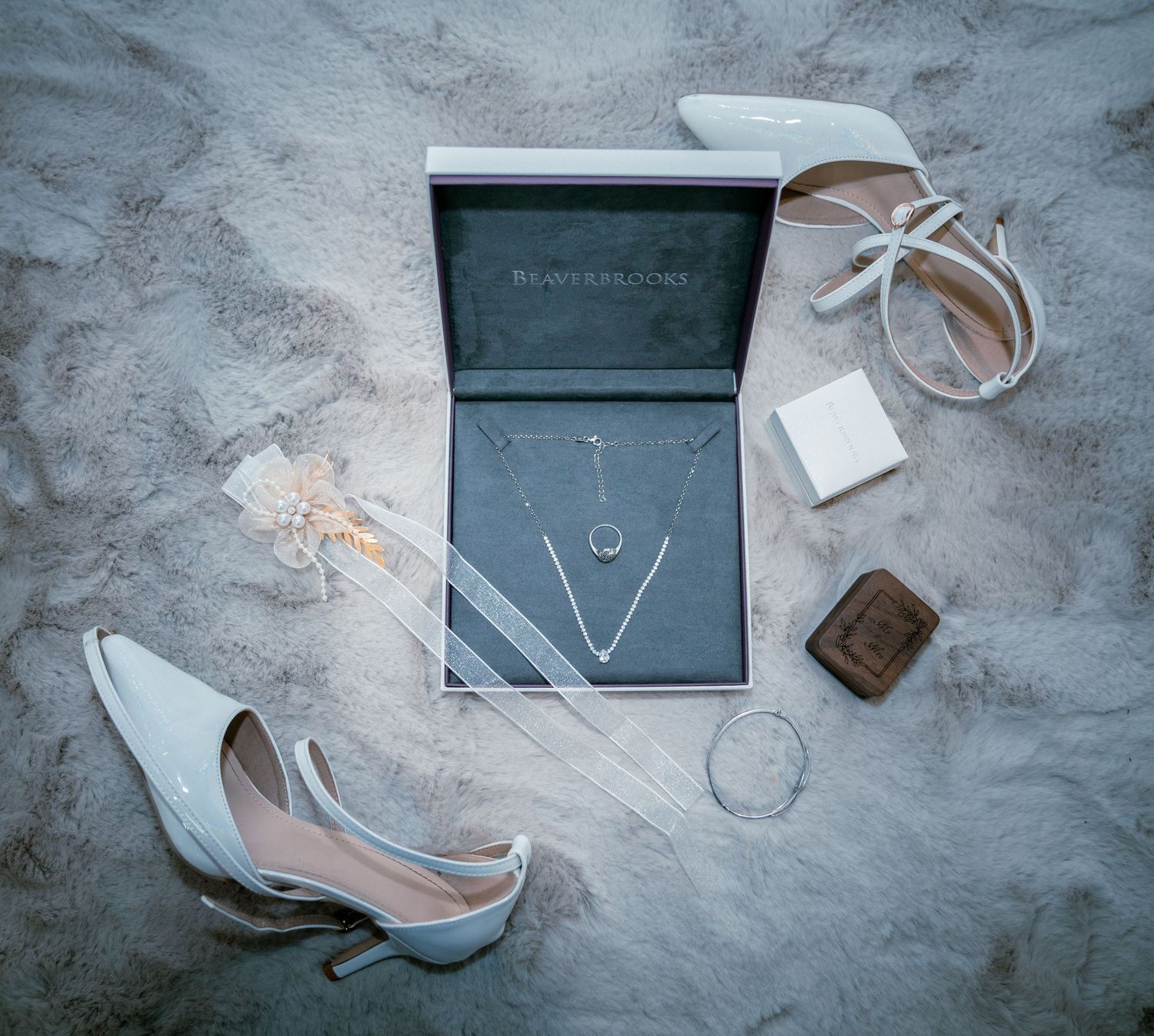 Elegant bridal accessories flatlay featuring white heels, necklace, rings, and jewelry box on marble.