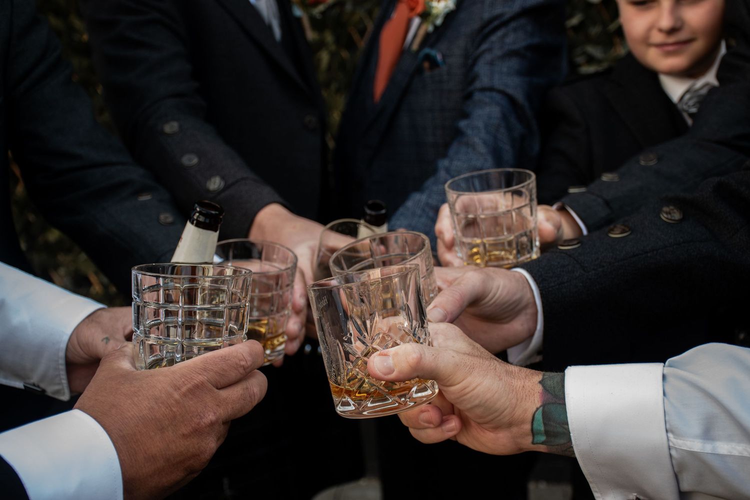 Groomsmen toasting with whiskey glasses in a close-up shot at a wedding celebration.