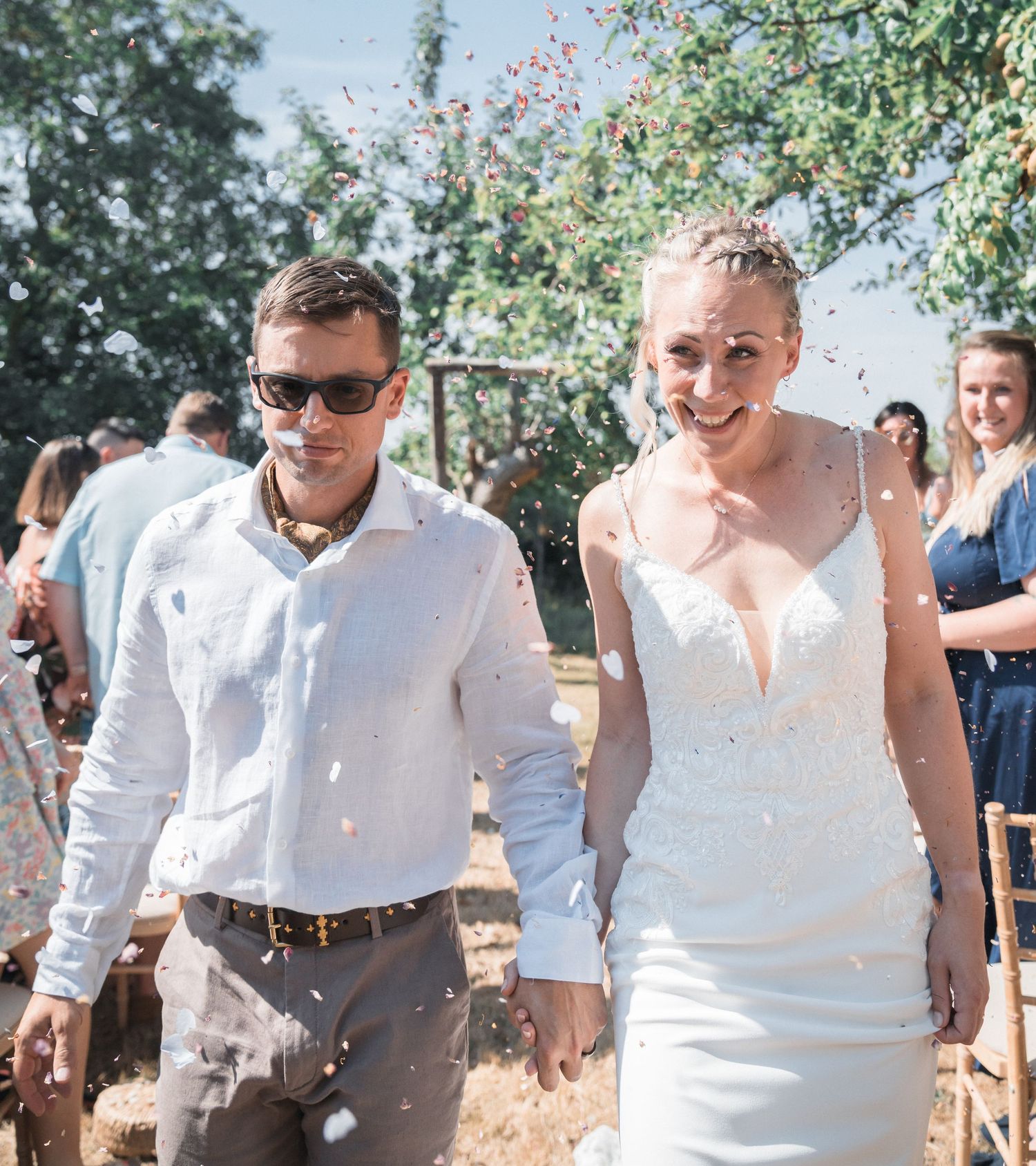 Happy newlyweds walking through a shower of colorful confetti outdoors on a sunny wedding day.