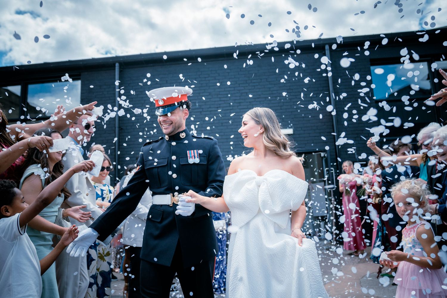 Military groom in dress uniform and bride exit ceremony through confetti shower.
