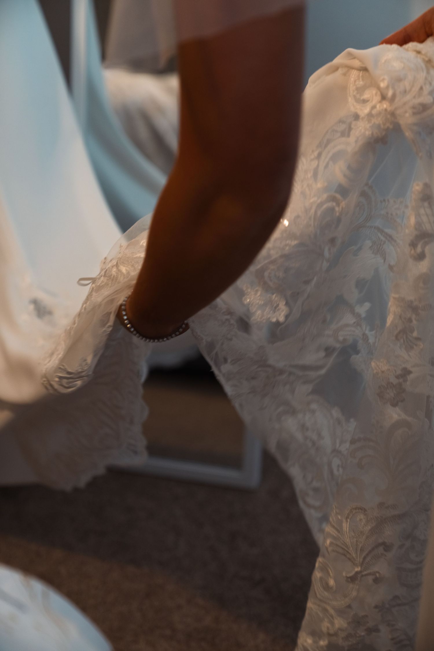 Close-up detail of a hand adjusting an intricate beaded and embroidered white wedding dress.