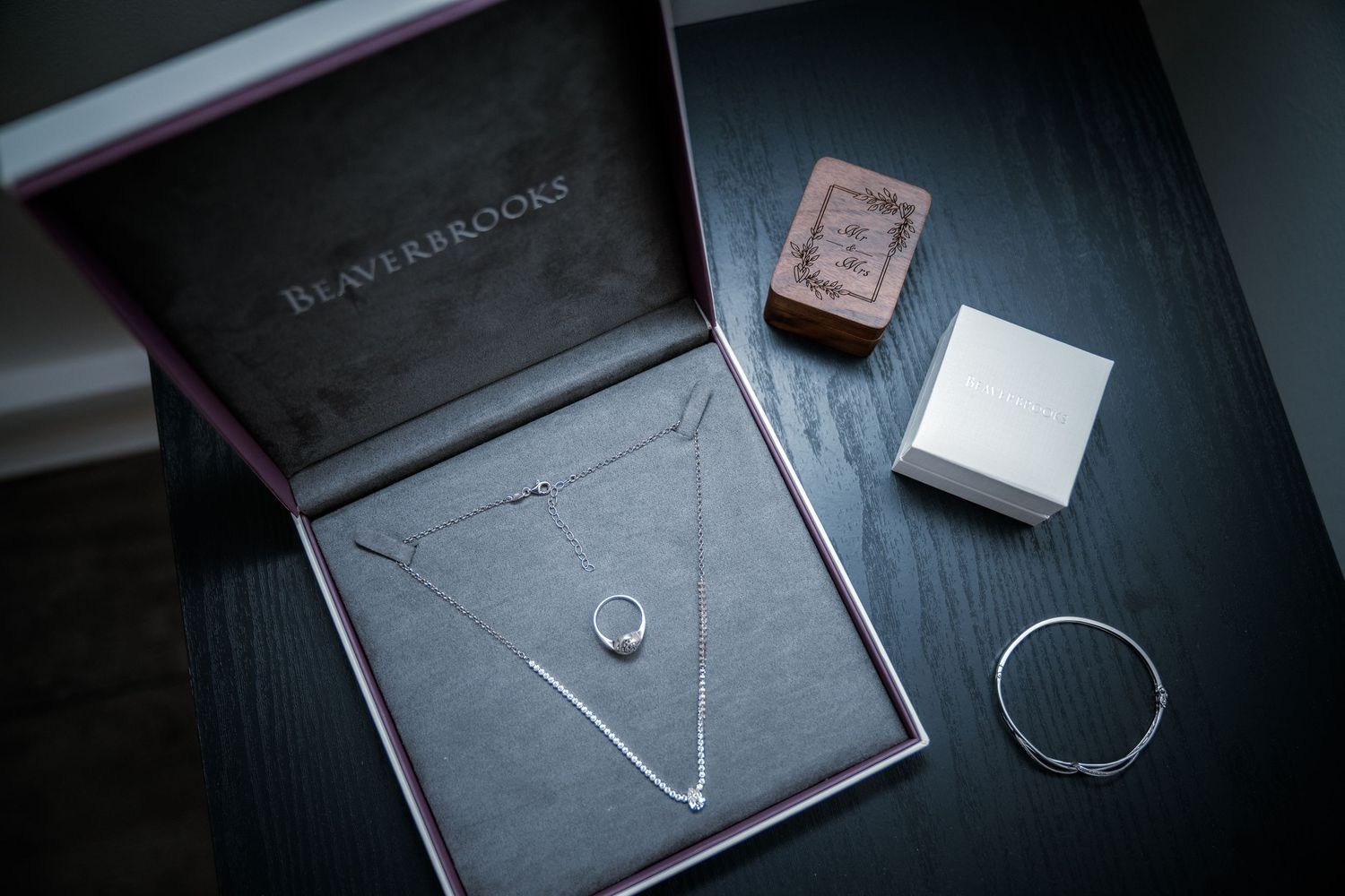 Beaverbrooks jewelry box with silver necklace, bracelet, and ring boxes on dark table.