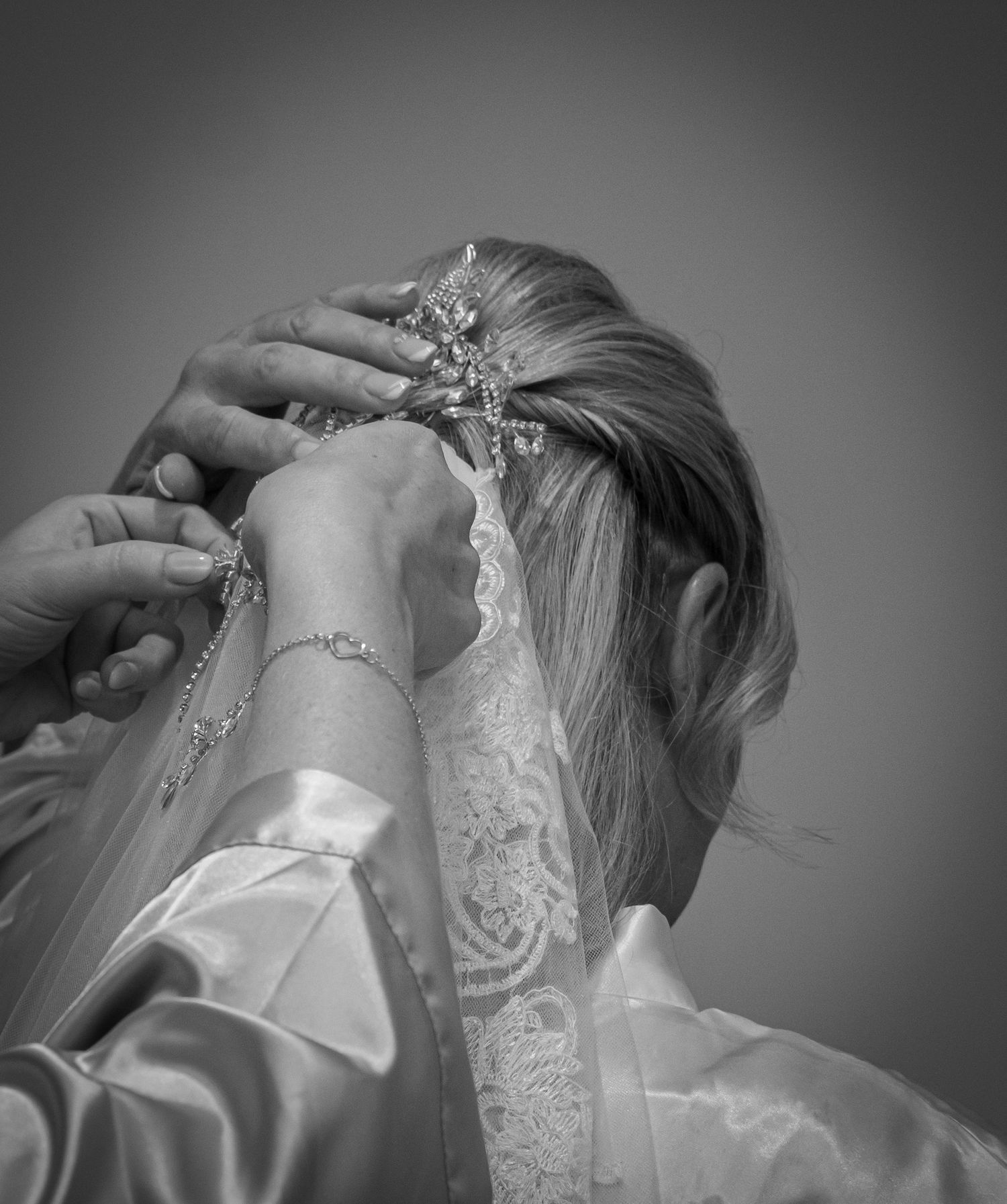 Black and white photo of hands pinning a decorative hair accessory and veil into brides updo.