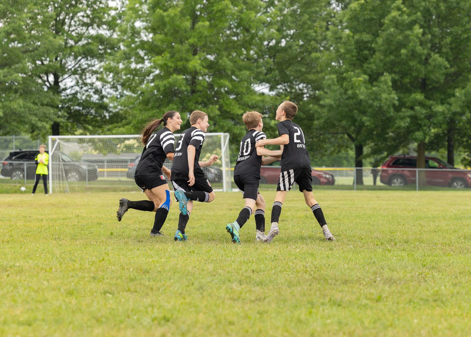action sports group shot after a goal 3 male 1 female soccer players wearing black uniforms celebrating a goal together at half field