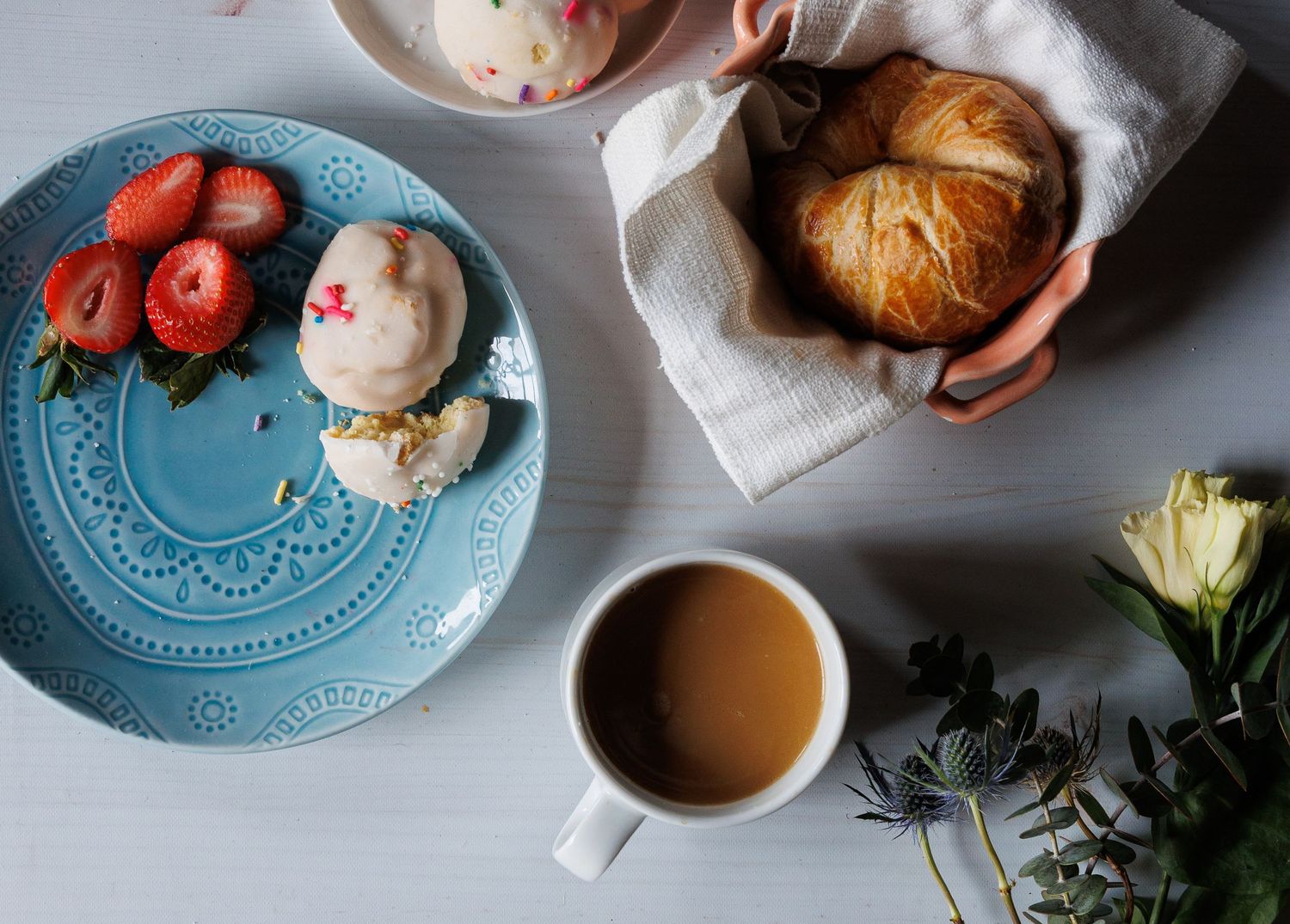 still life image of pastries strawberries in and on colored plates coffee and white rose on a white washed wood panel background