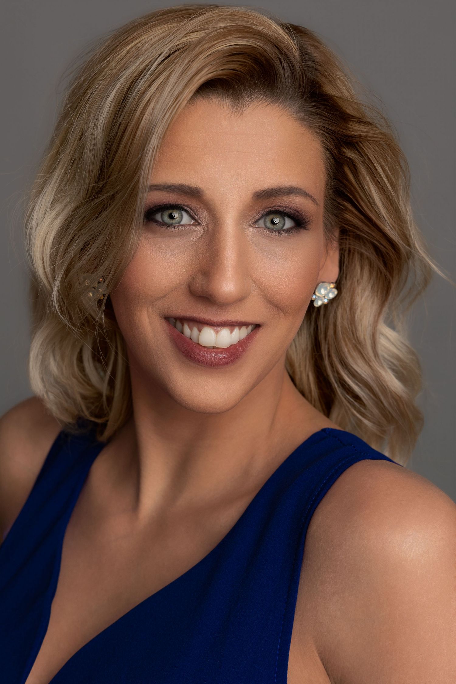 close up headshot of a blonde female wearing a blue tank top and big jewelry