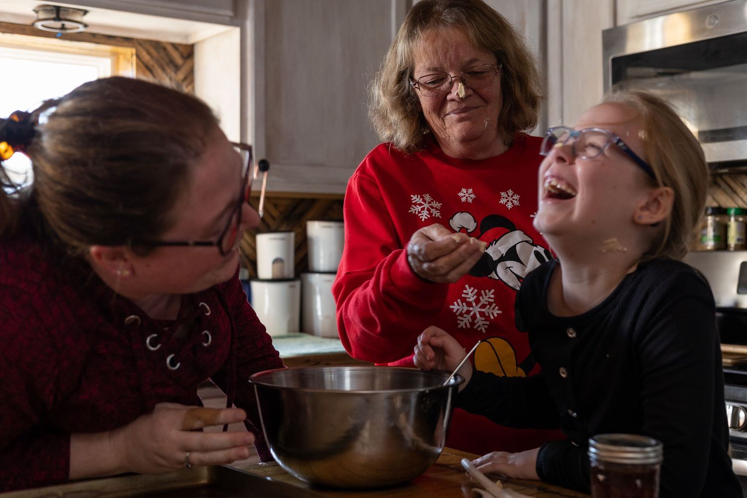 horizontal family image 3 generations of women mixing cookies in a kitchen laughing and joking about putting batter on each others noses
