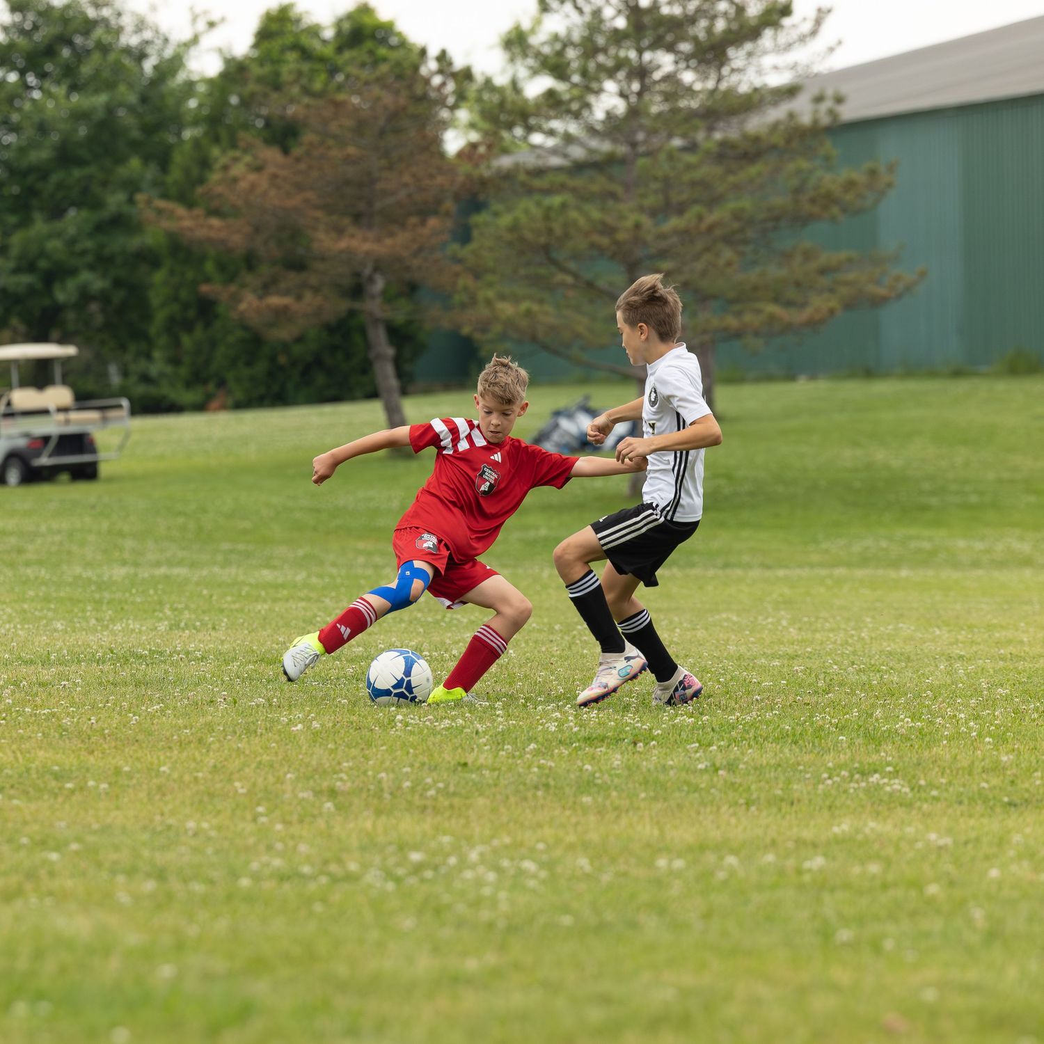 action sports game soccer young boy player wearing red uniform kicking ball away from male player wearing white and black uniform
