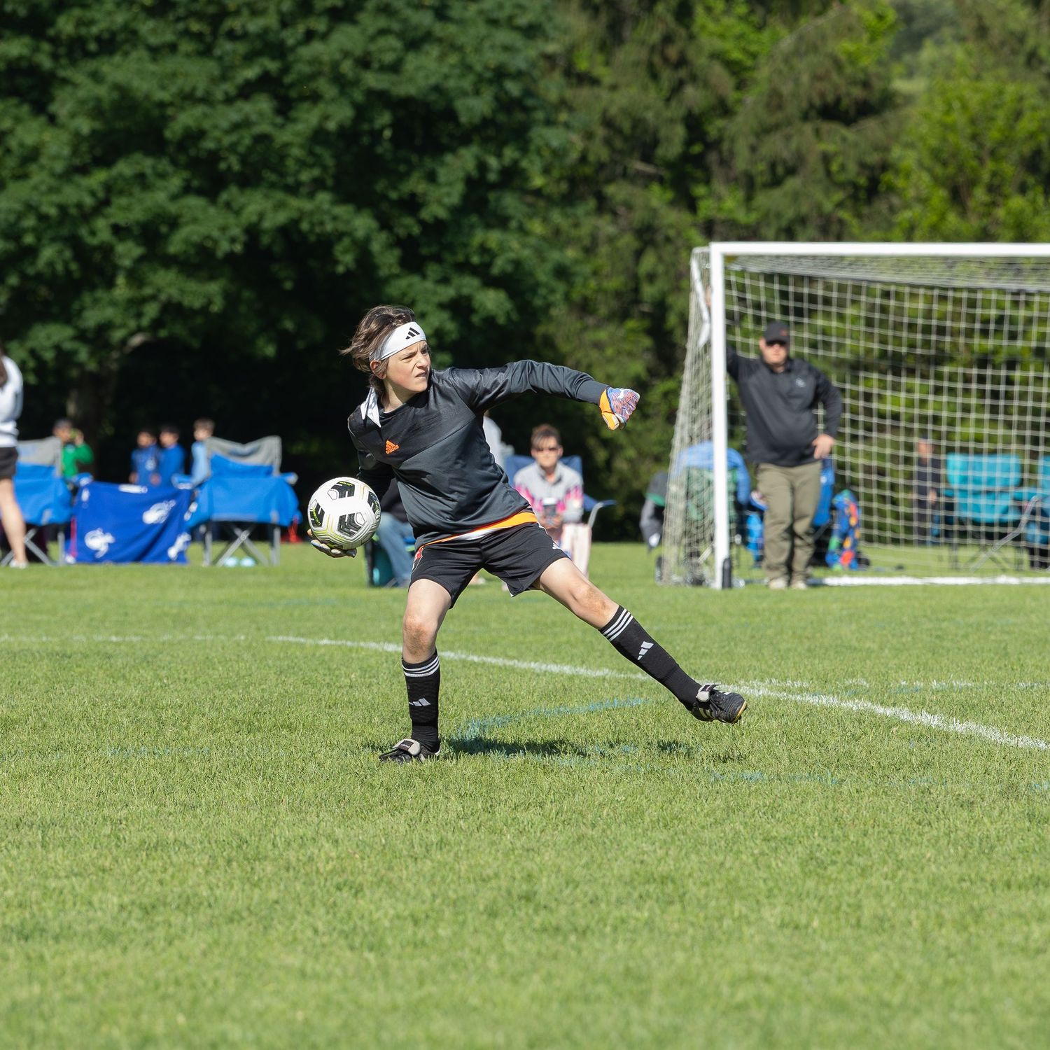 action sports soccer game goal keeper wearing black uniform and white hair band out of the goal pulling an arm back to throw soccer ball