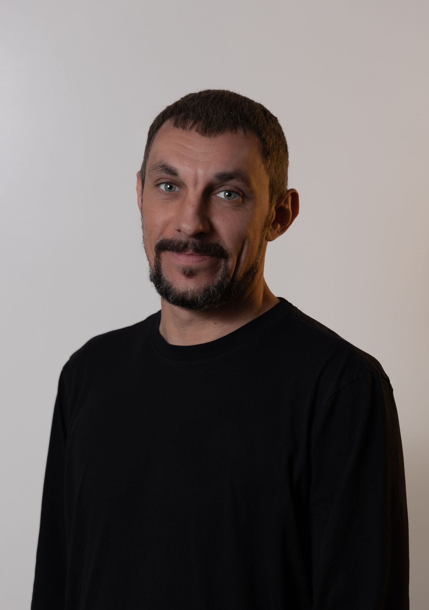 headshot of a short haired, bearded brunette male in a black long sleeve shirt in front of a white backdrop