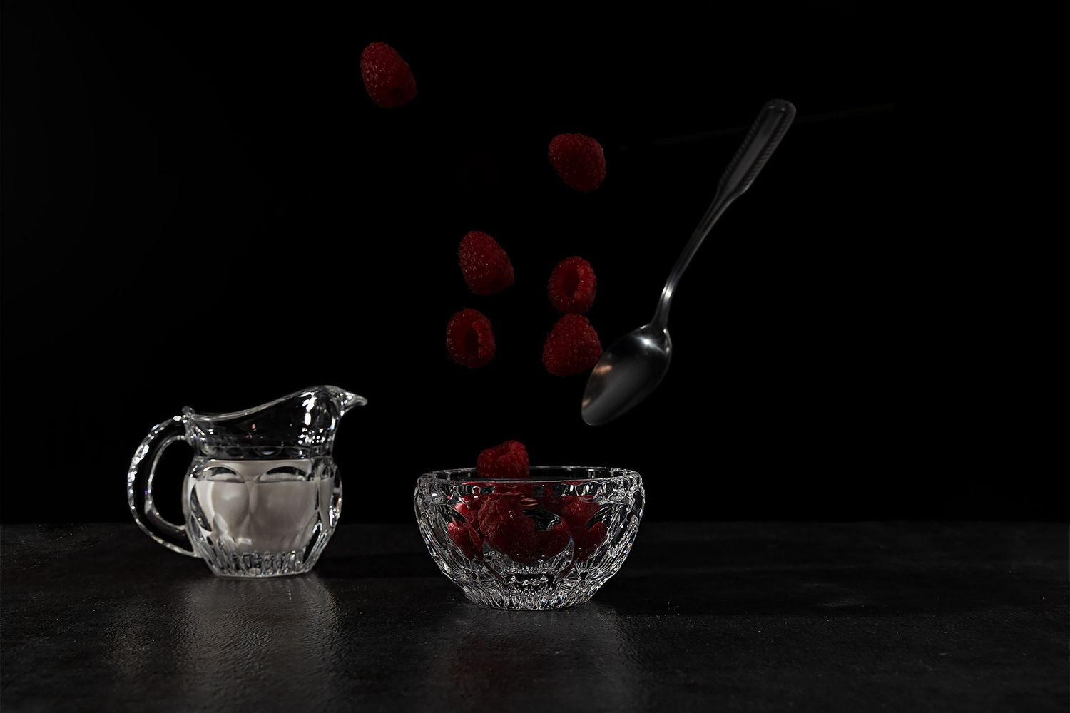 still life image of a mini crystal pitcher filled with cream next to a mini crystal bowl with raspberries falling in to it and a spoon