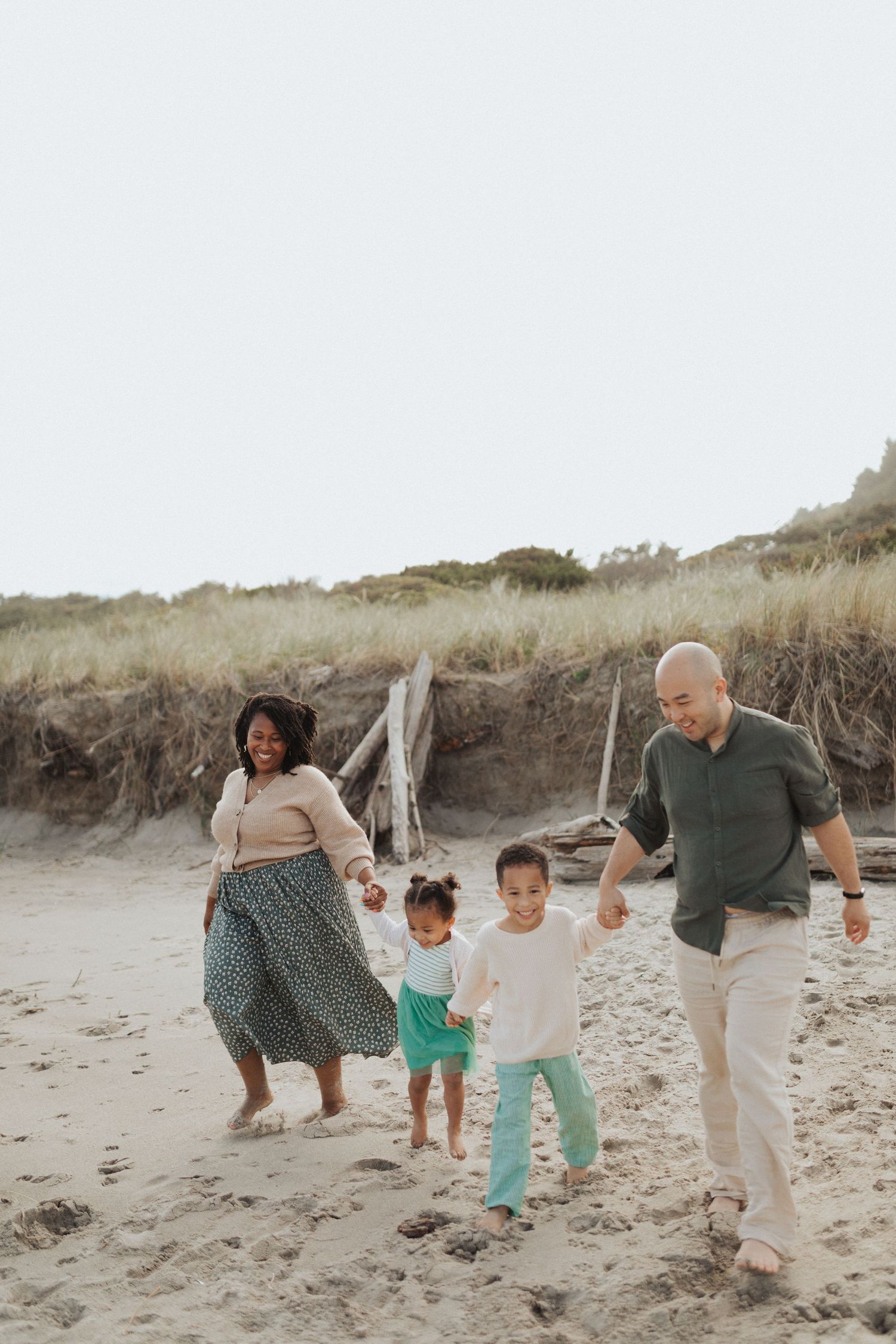 Joyful interracial family with two young children walking hand in hand on a sandy beach.