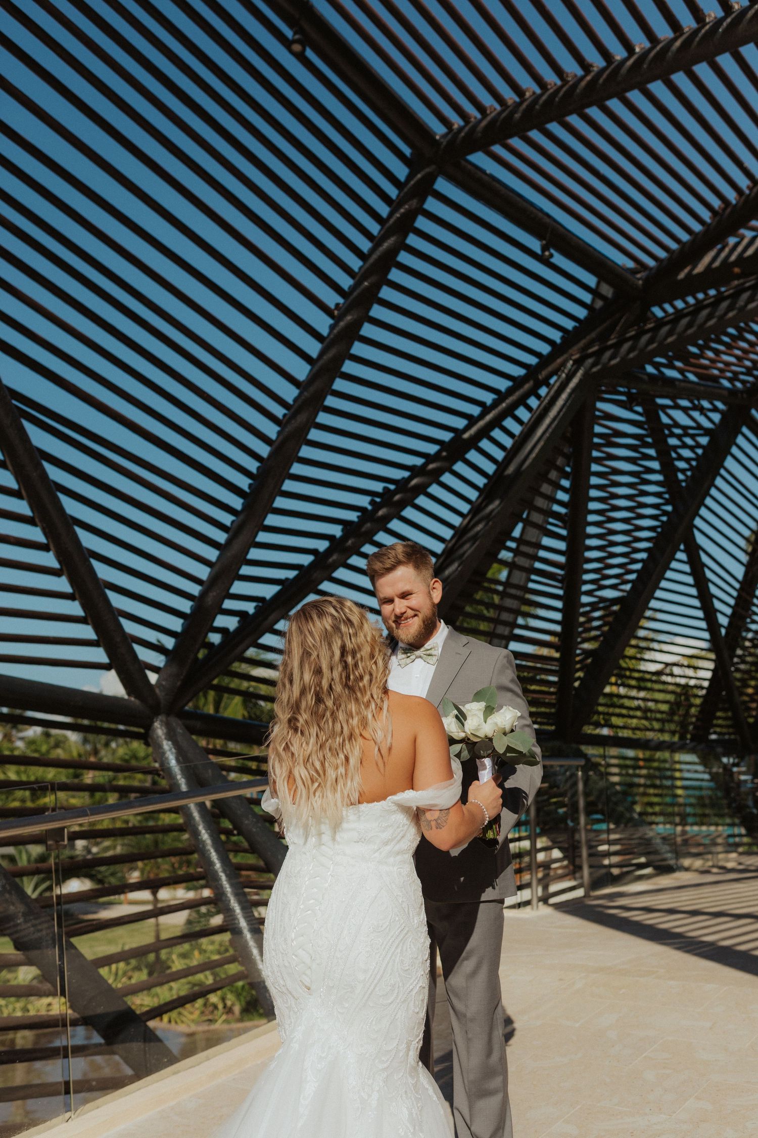 Bride and groom sharing romantic moment under geometric metal lattice structure at wedding venue.